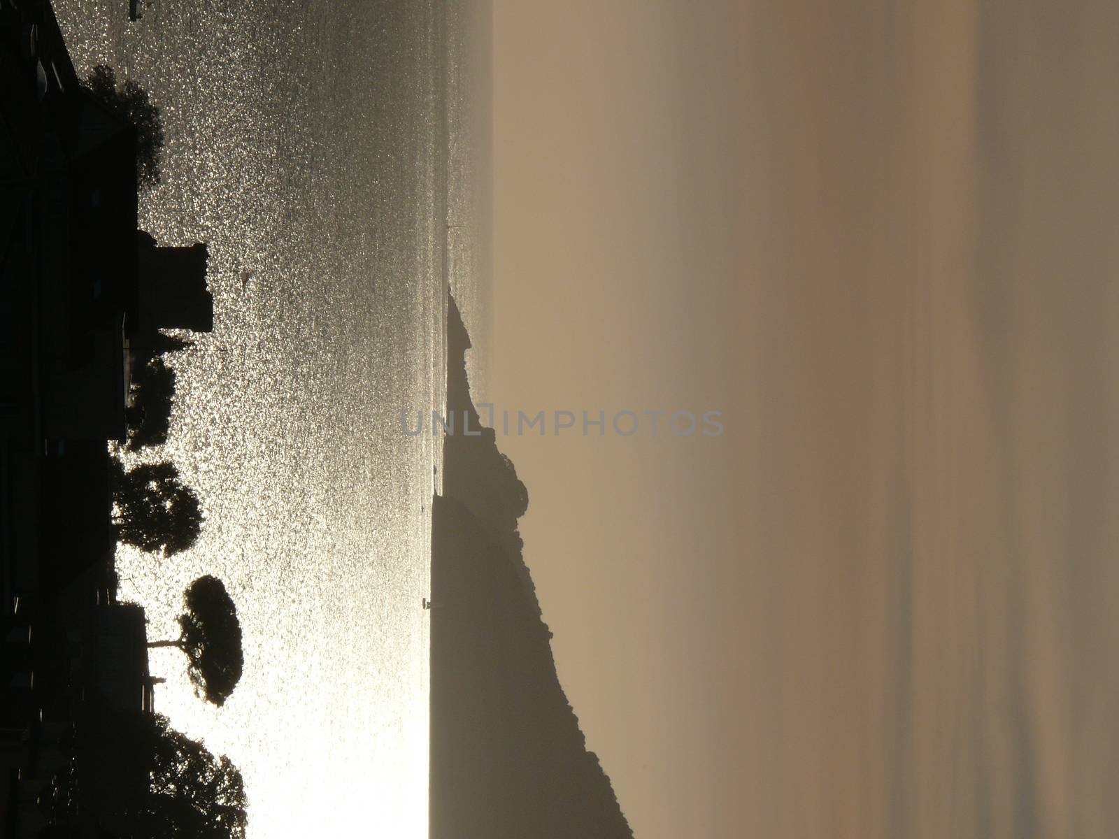 Silhouette of San Terenzo castle at sunset. Sky with clouds and sea of gold color.