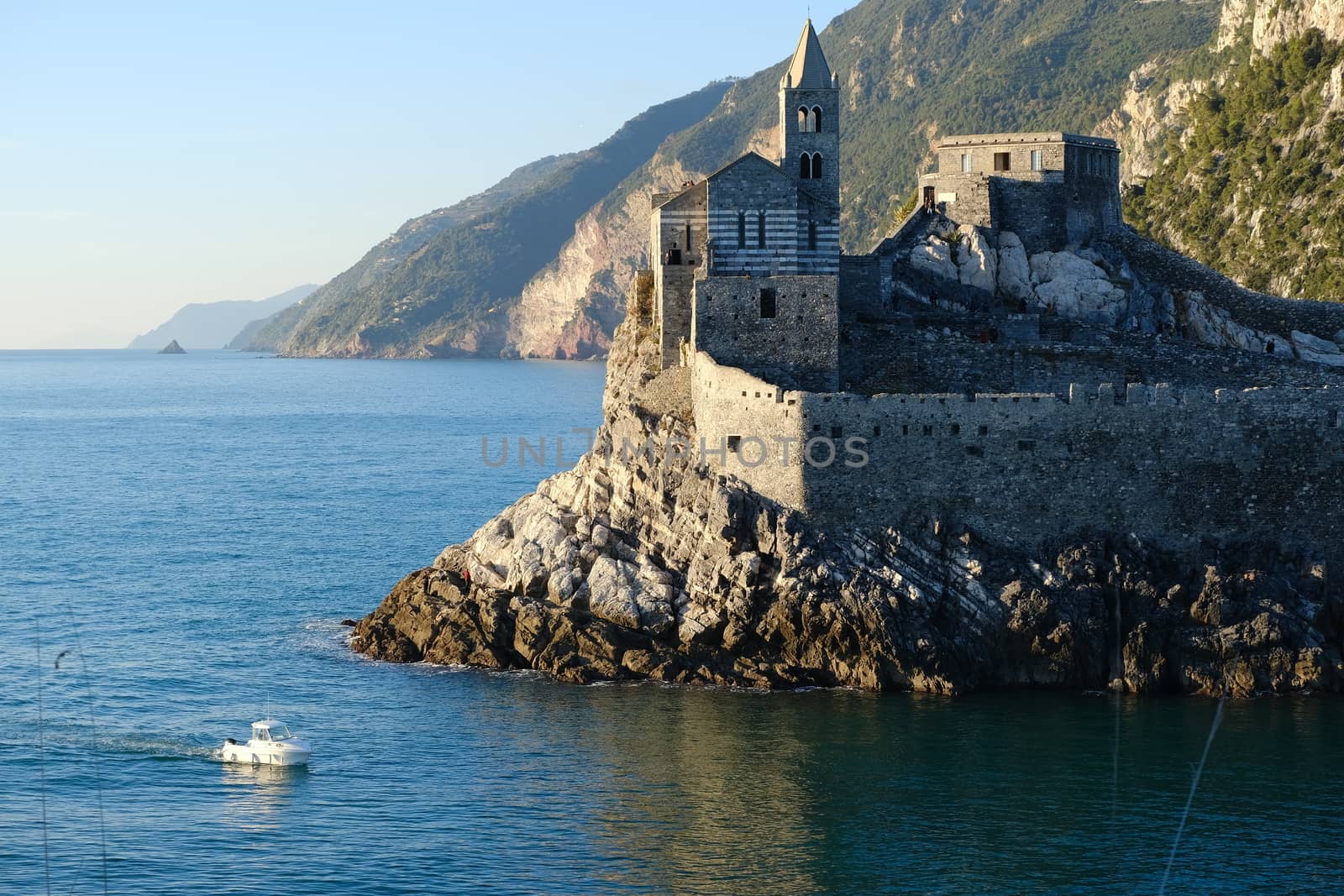 Portovenere, La Spezia, Italy. About 12/2019. Church of San Pietro in Portovenere on the rocks overlooking the sea. White boat in the sea and rocks near the Cinque Terre in Liguri. Italy.