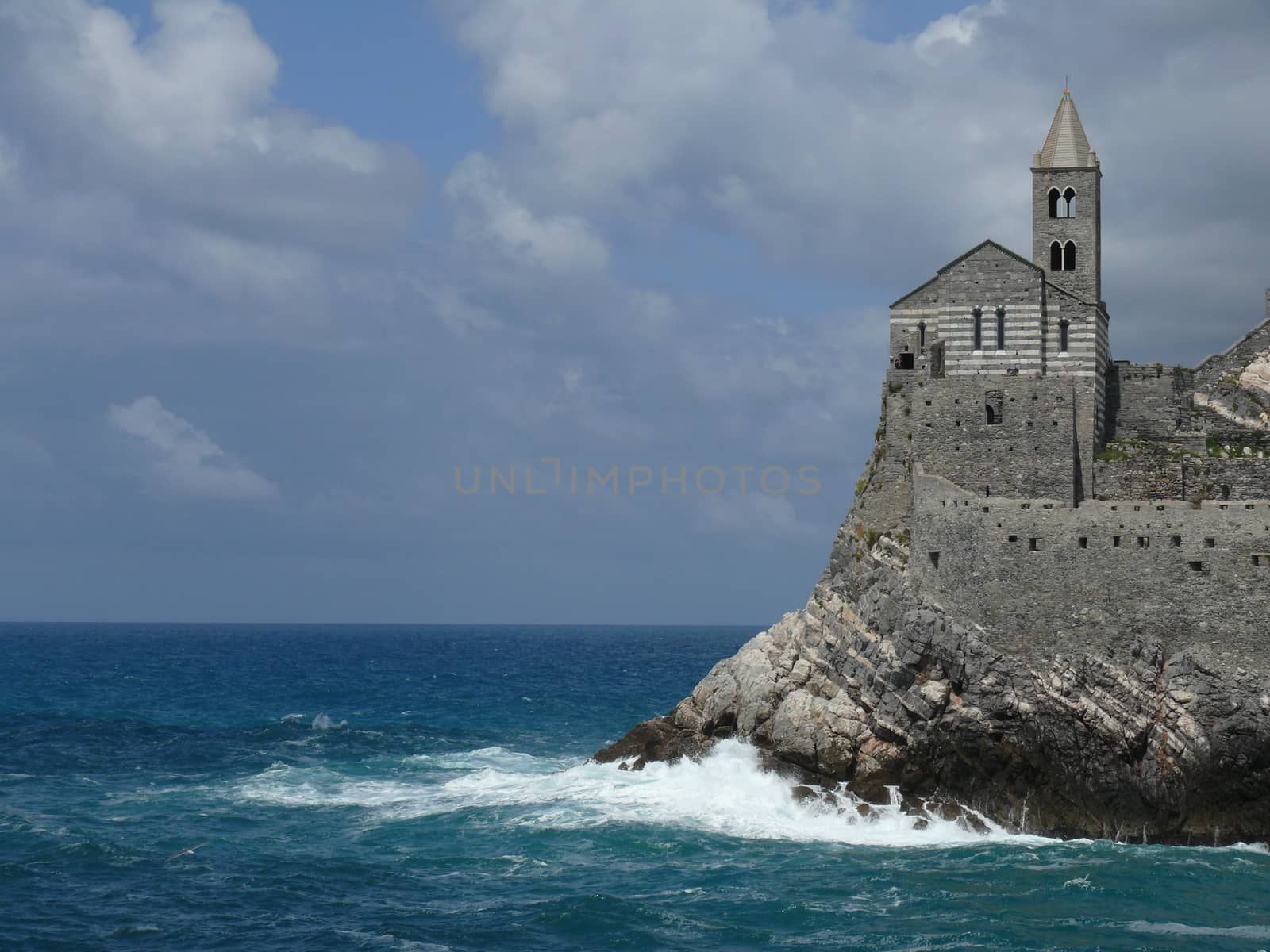 Church of San PIetro in Portovenere, built on a rock overlooking the sea. Sky with clouds and blue sea waves.