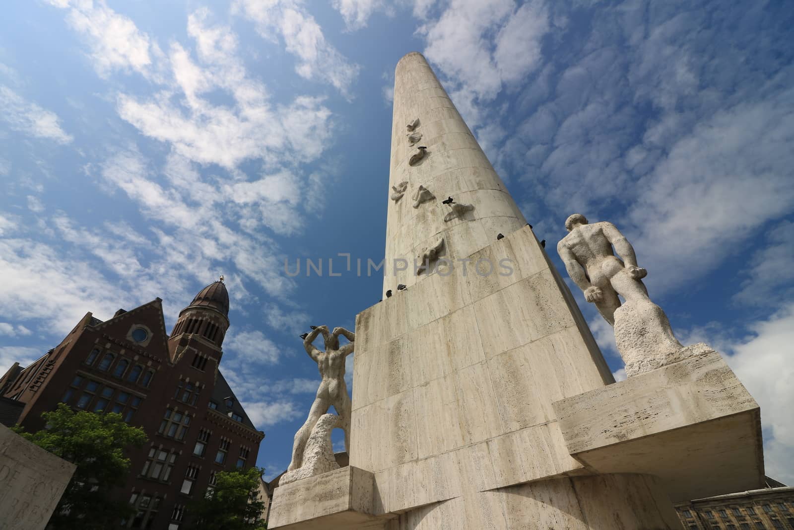 Amsterdam, Netherlands. About the July 2019. Monument in Dam square. In the background the ancient buildings. Blue sky with white clouds.