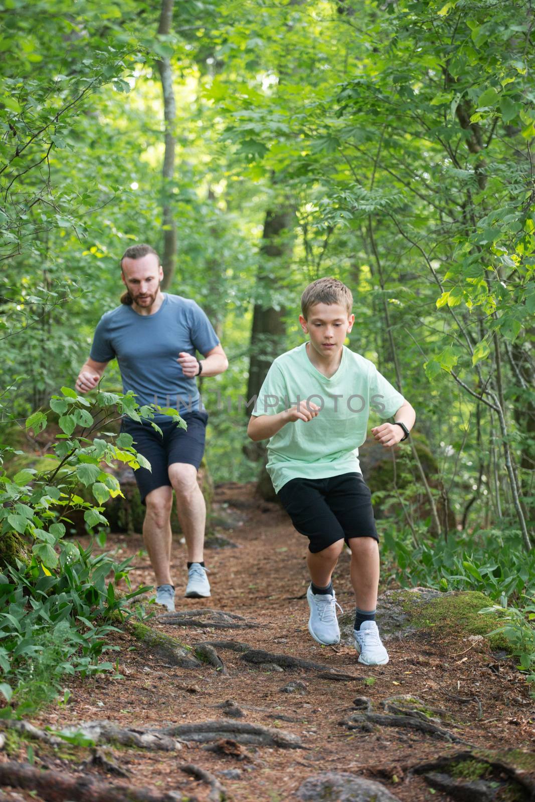 Father and son run in forest by destillat