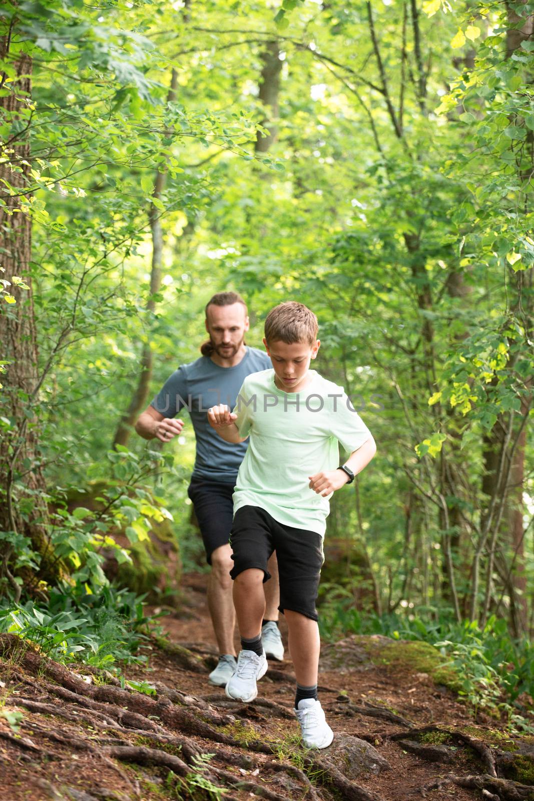 Father and son run in forest by destillat