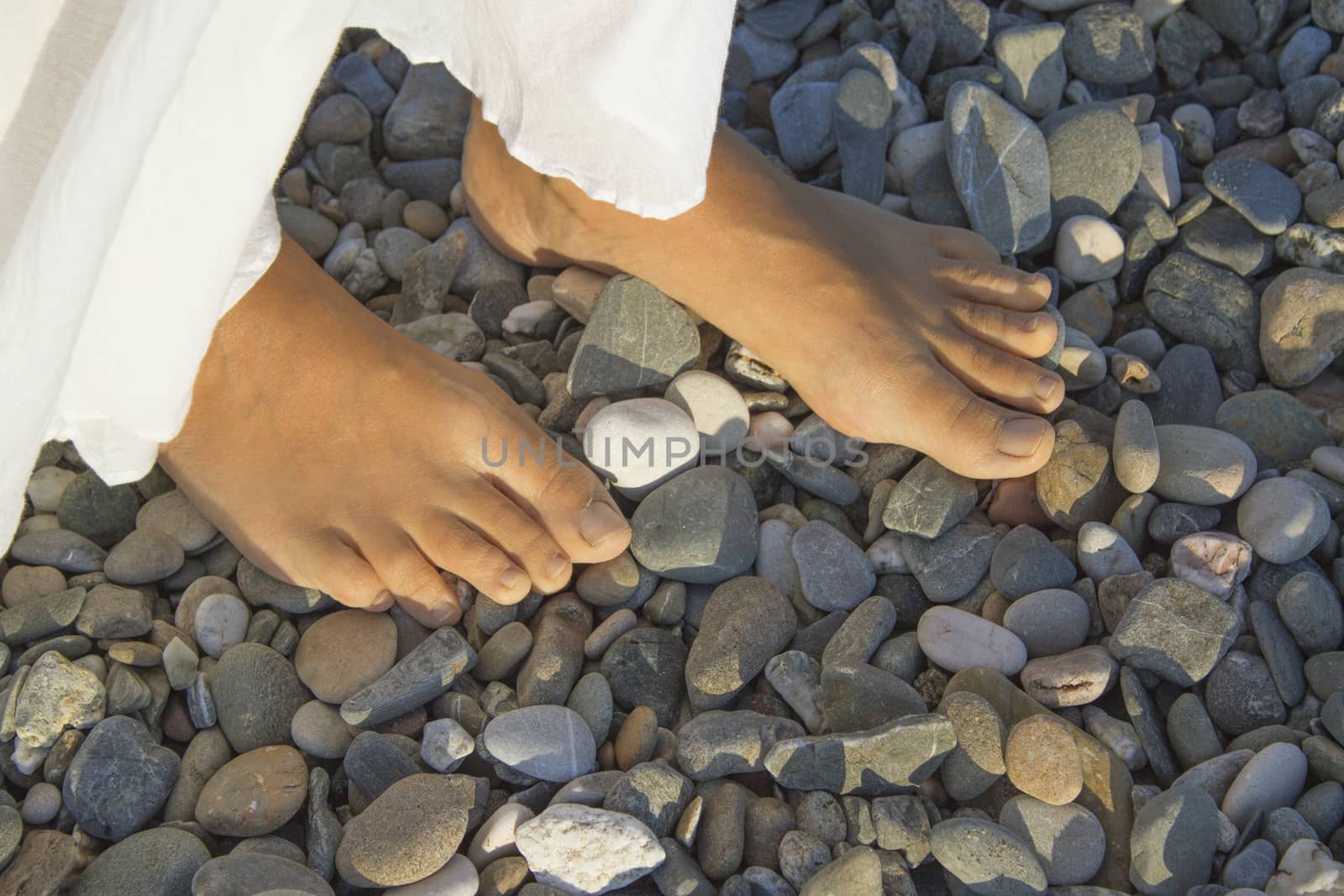 Feet of young woman on pebble beach. Part of a white skirt