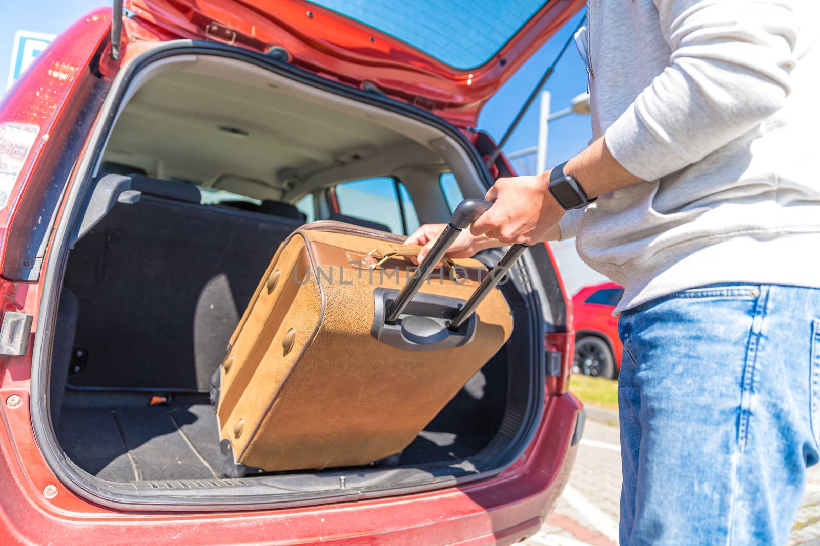 A young man puts luggage in the trunk of a car.