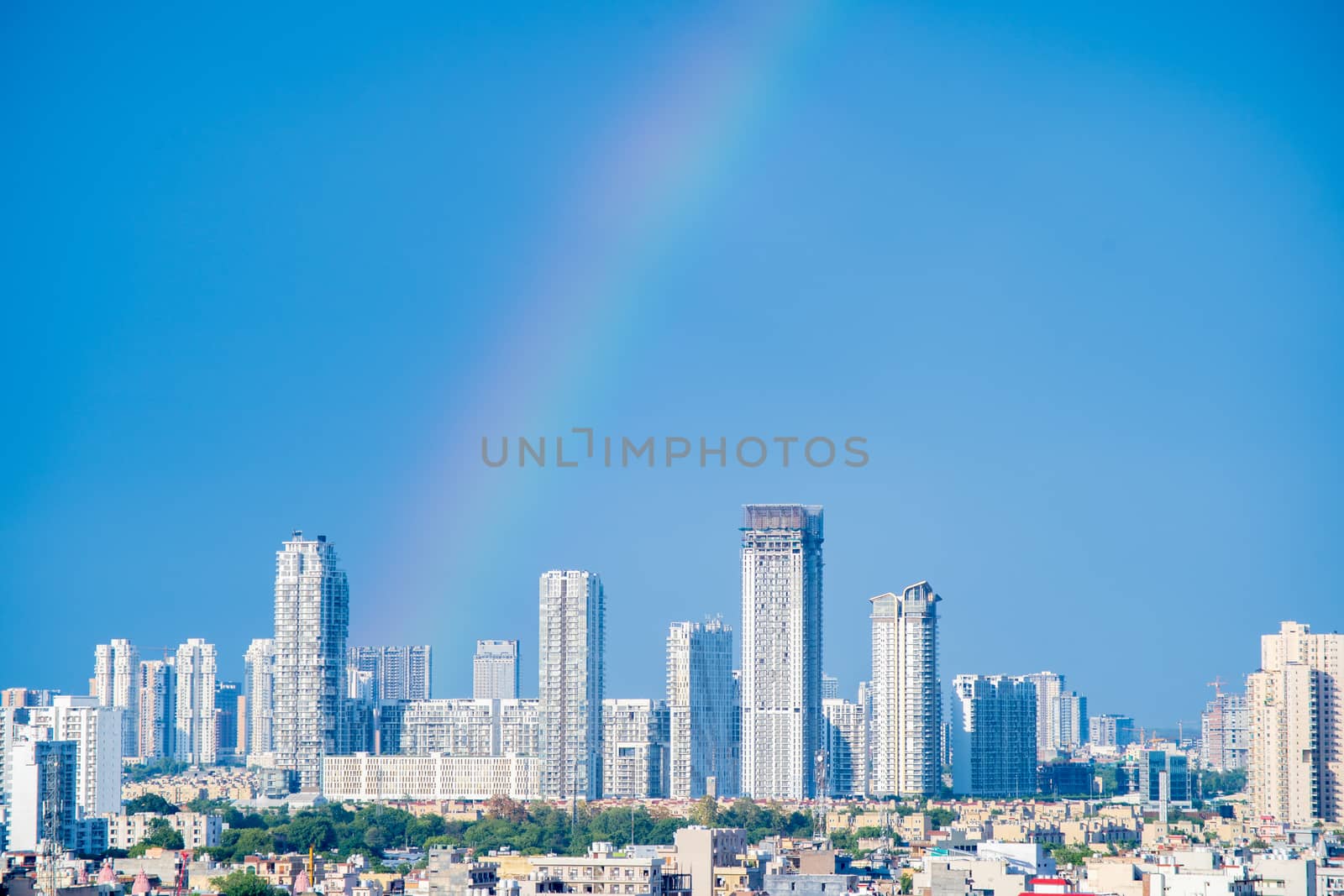 Aerial cityscape shot of buildings in gurgaon delhi noida with a rainbow behind them on a monsoon day. Shows the natural phenomenon in Jun 2020 where a double rainbow was seen in the indian capital