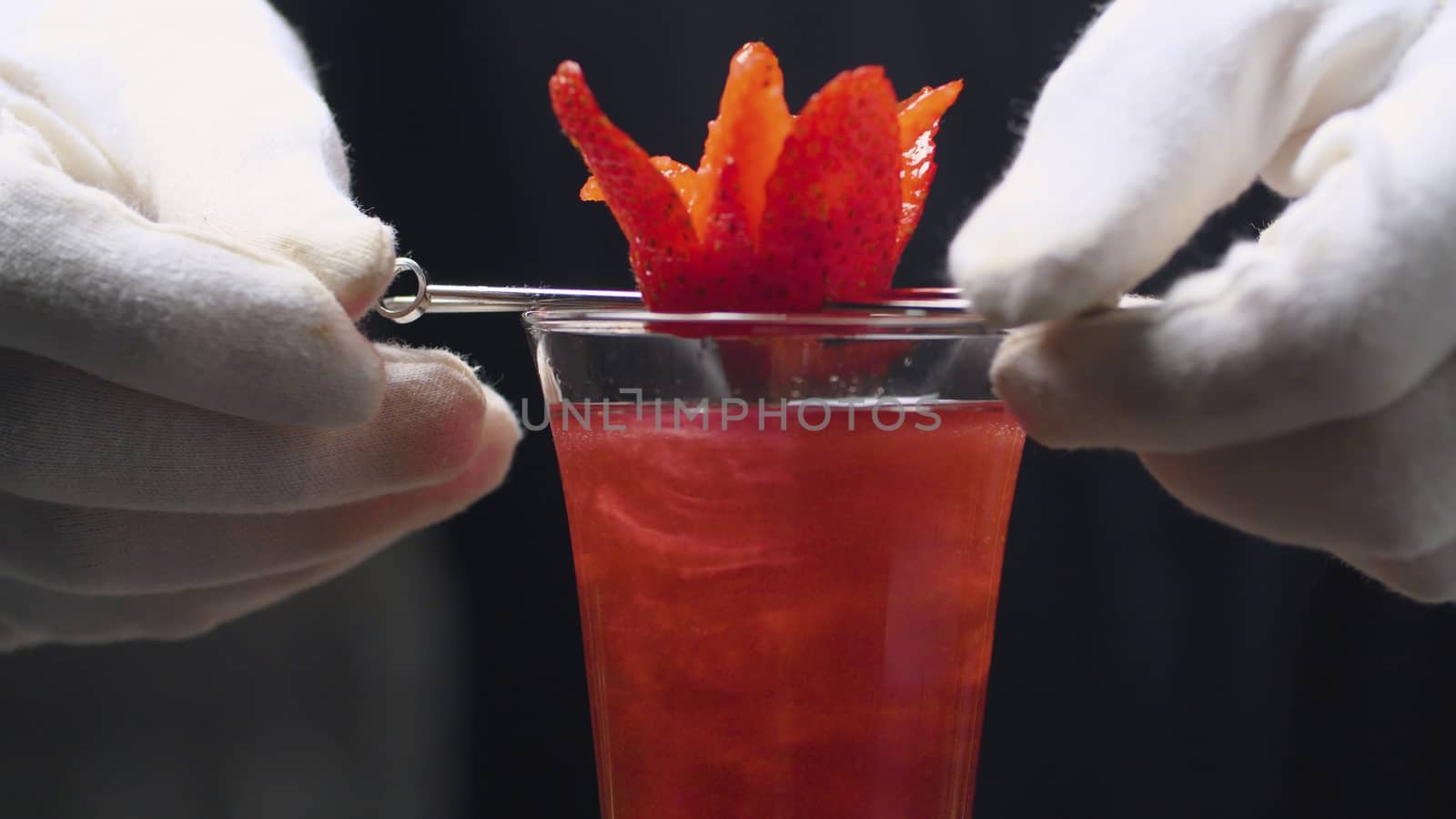 Making Strawberry Rossini Cocktail. Close up bartenders hands put a strawberry flower on a skewer on the top of glass.