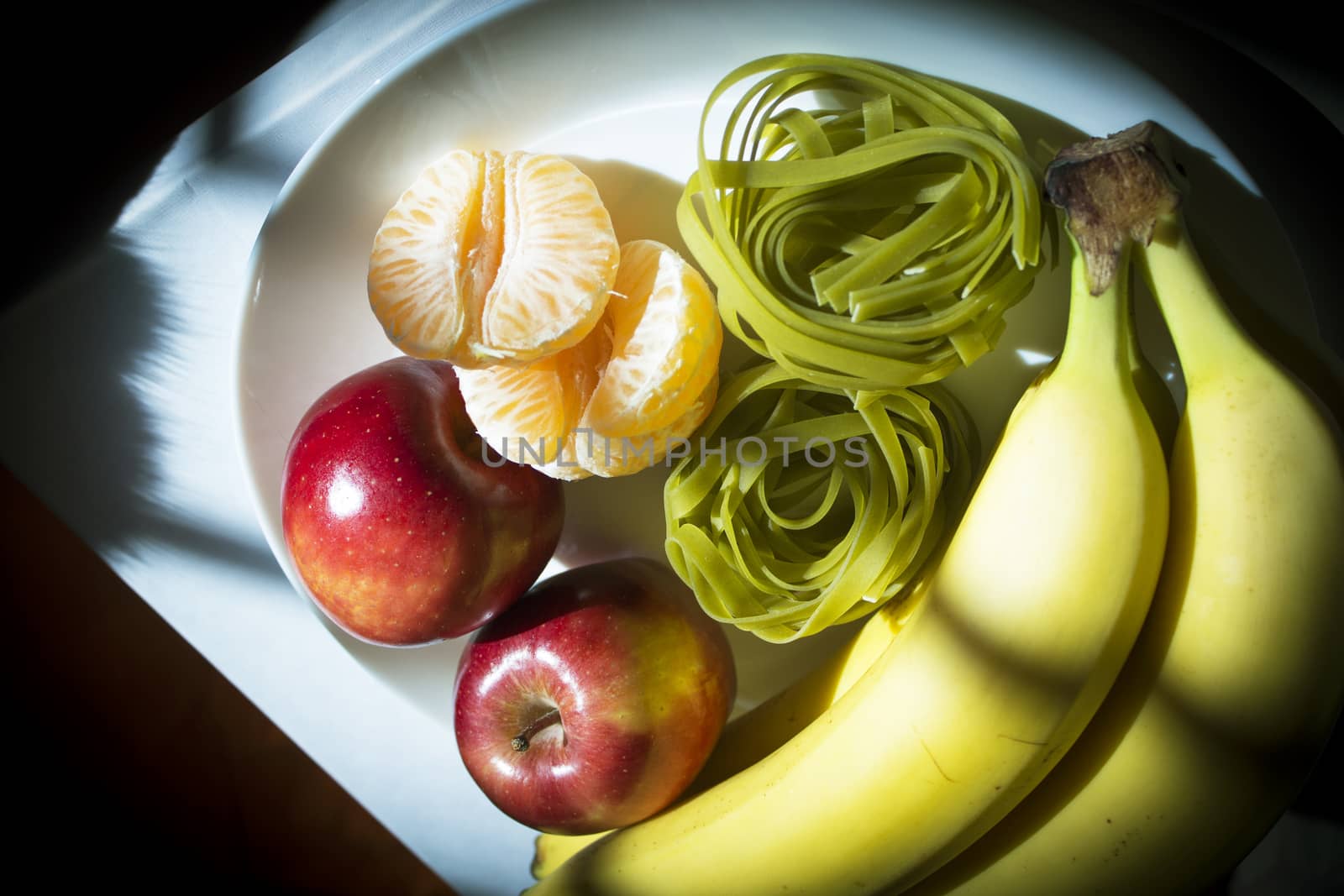 Plate with bananas, apples, tangerine and spinach pasta without cooking