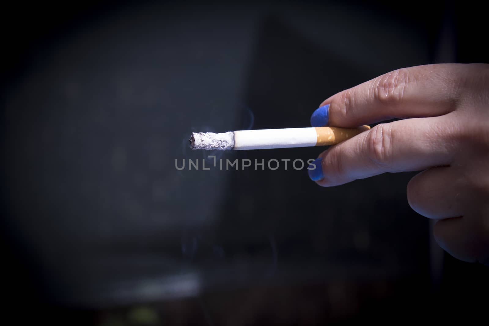 Womans hand holding lit cigarette. Dark background