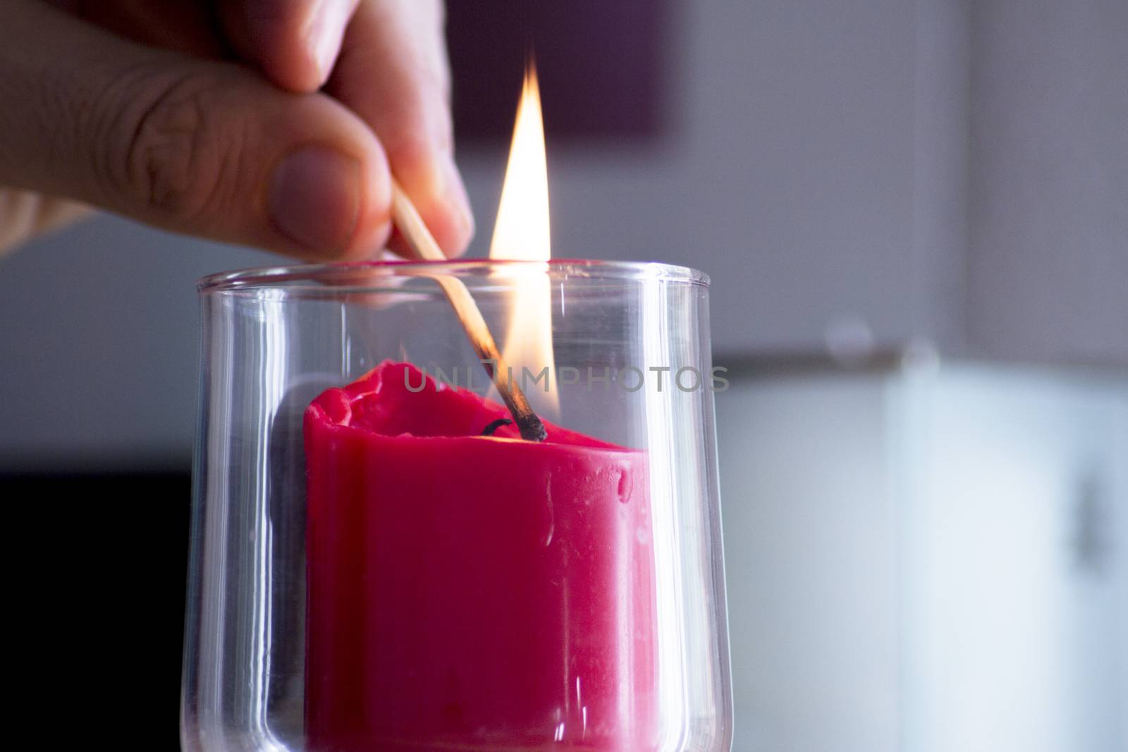 Fingers of man lighting a red candle inside a transparent glass vase with a match