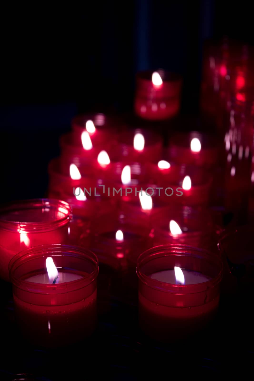 Many burning candles with red plastic sheath. No people