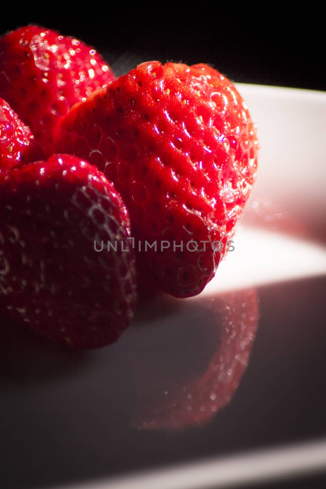 Ripe strawberries on a white plate and dark background. No people