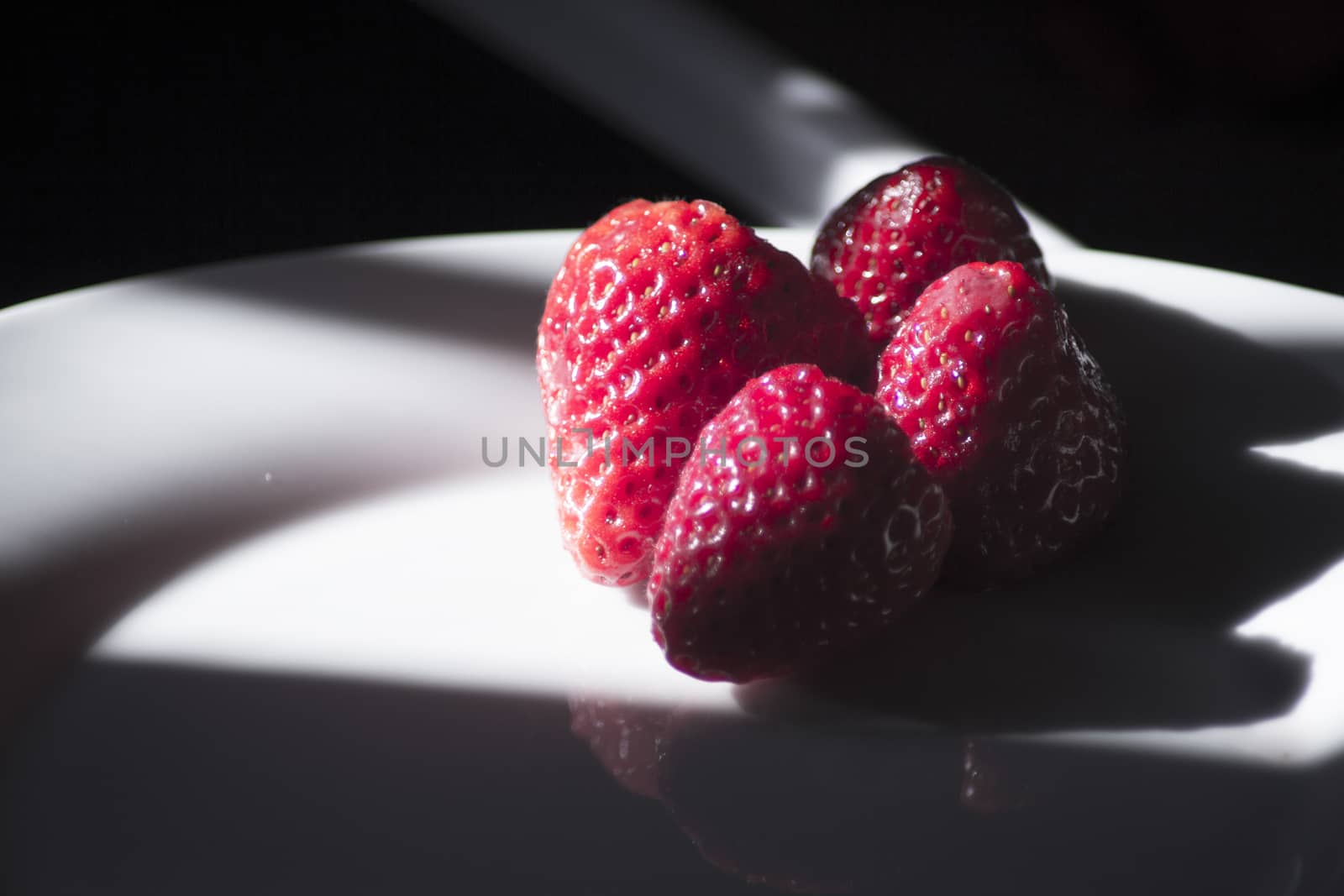 Ripe strawberries on a white plate and dark background. No people
