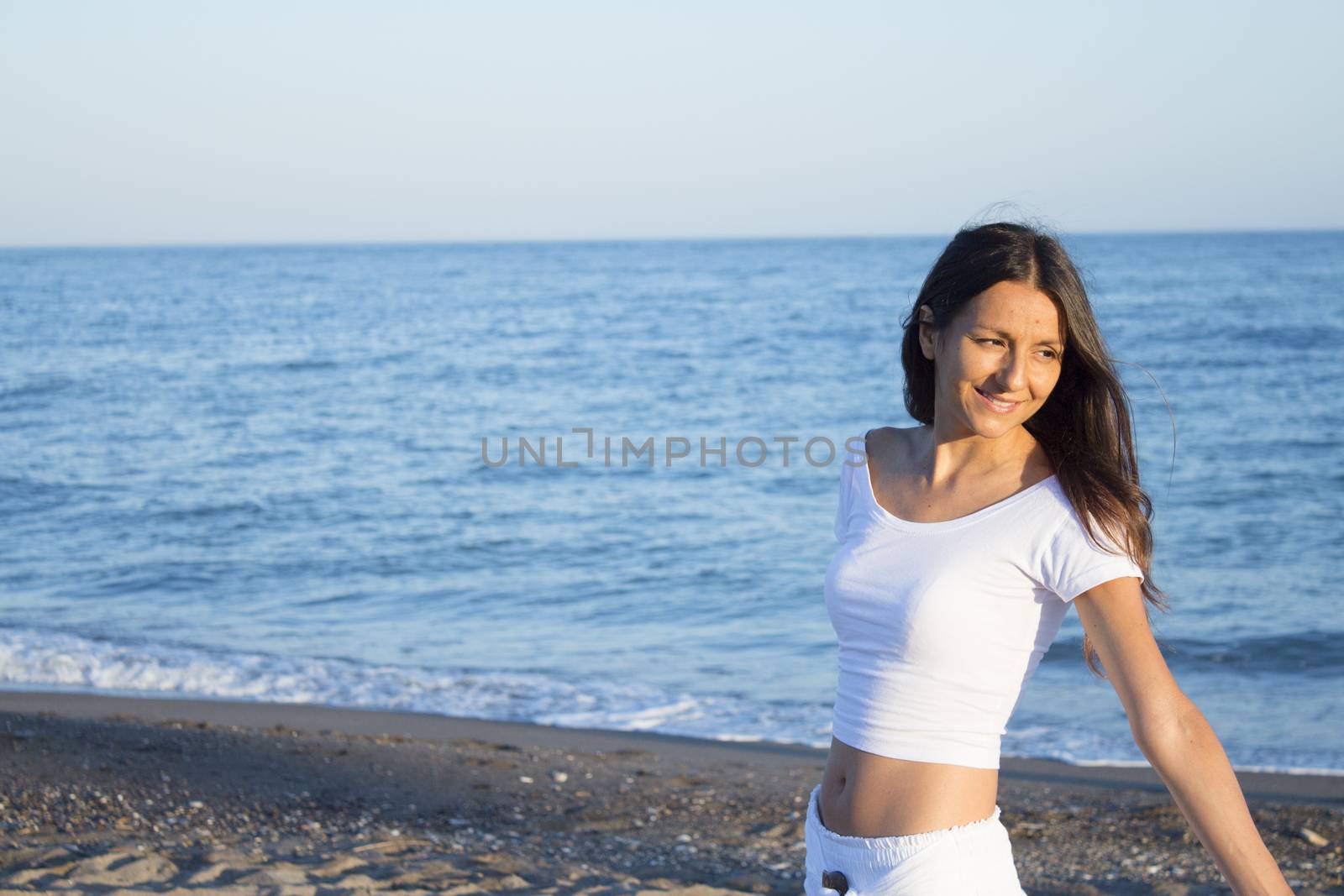 Woman dressed in white barefoot on the beach sand. Smiling