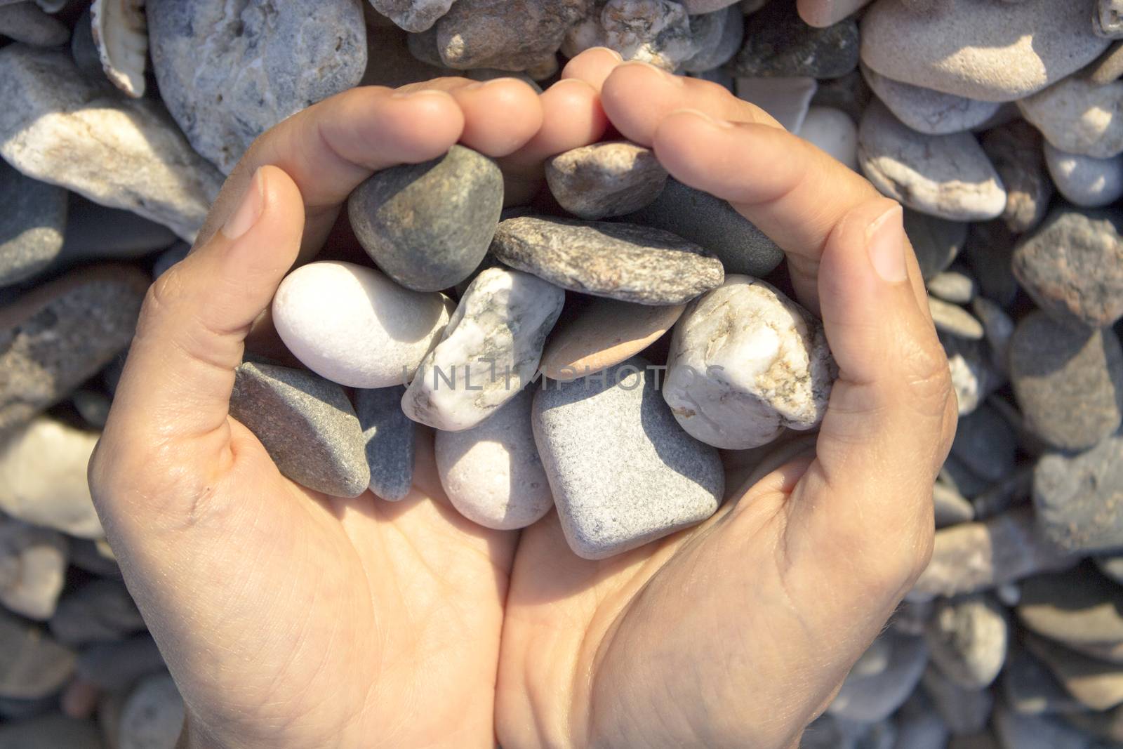 Woman hands touching stones on the beach. Grey stones