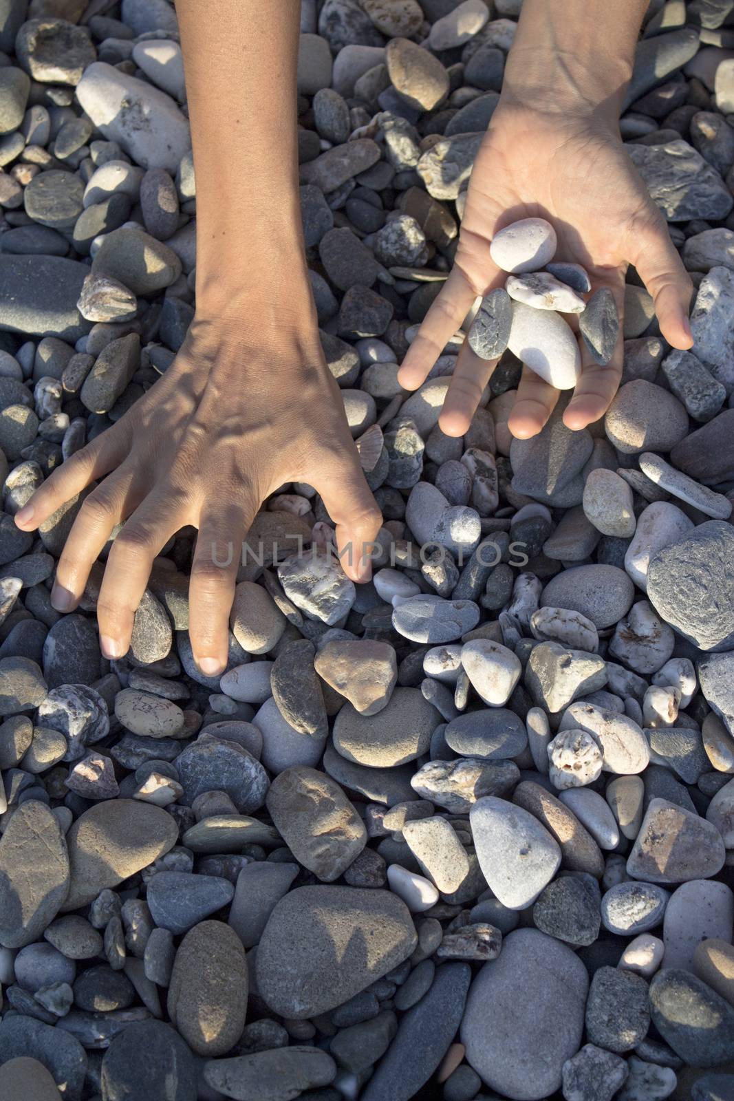 Woman hands touching stones on the beach. Grey stones