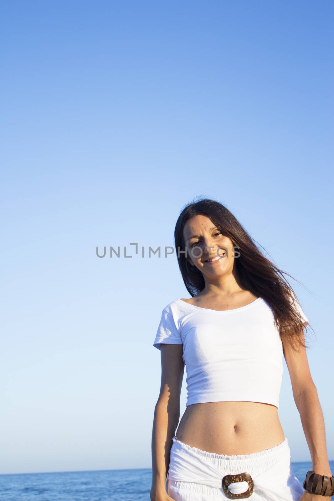 Woman dressed in white barefoot on the beach sand. Smiling