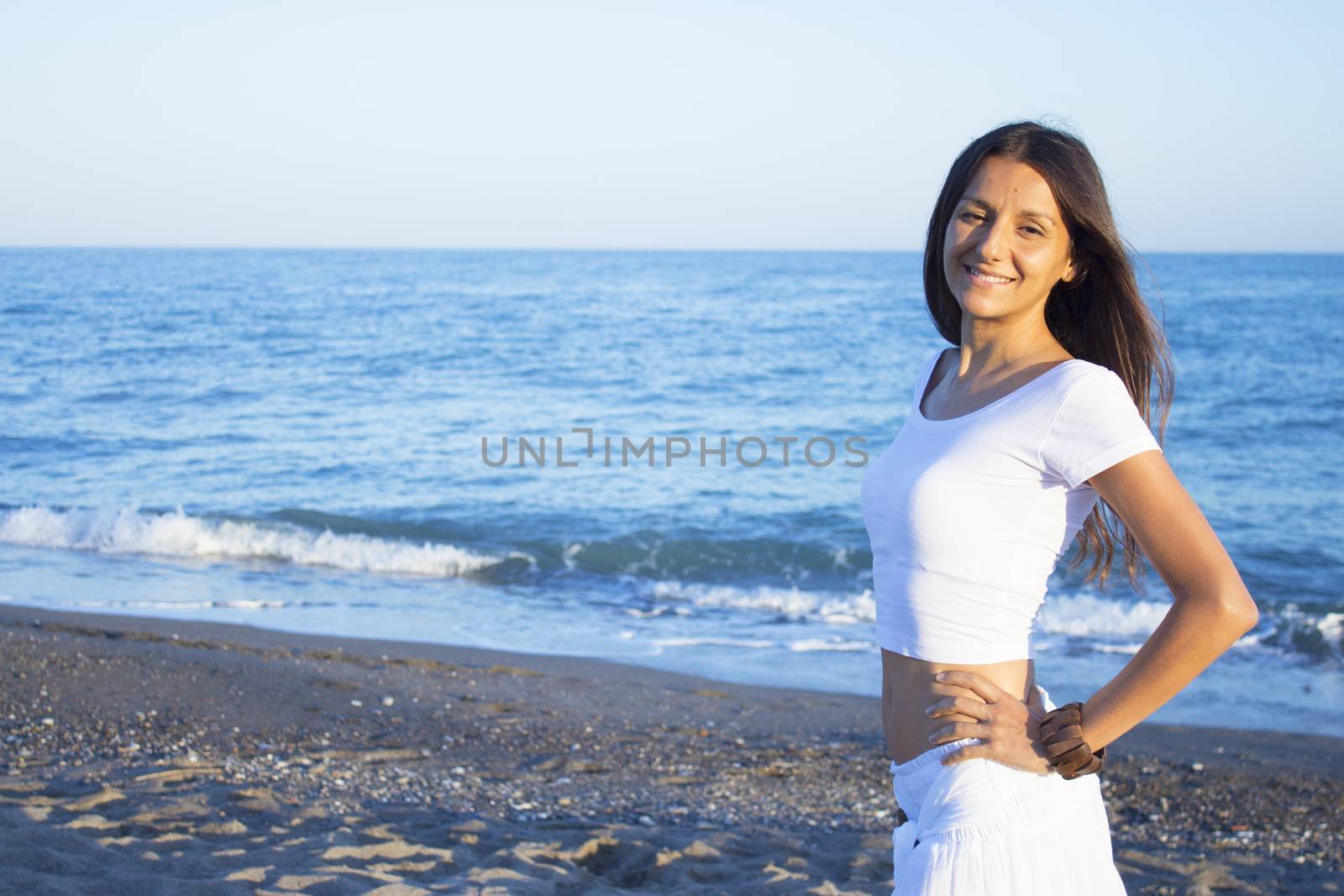 Woman dressed in white barefoot on the beach sand. Smiling