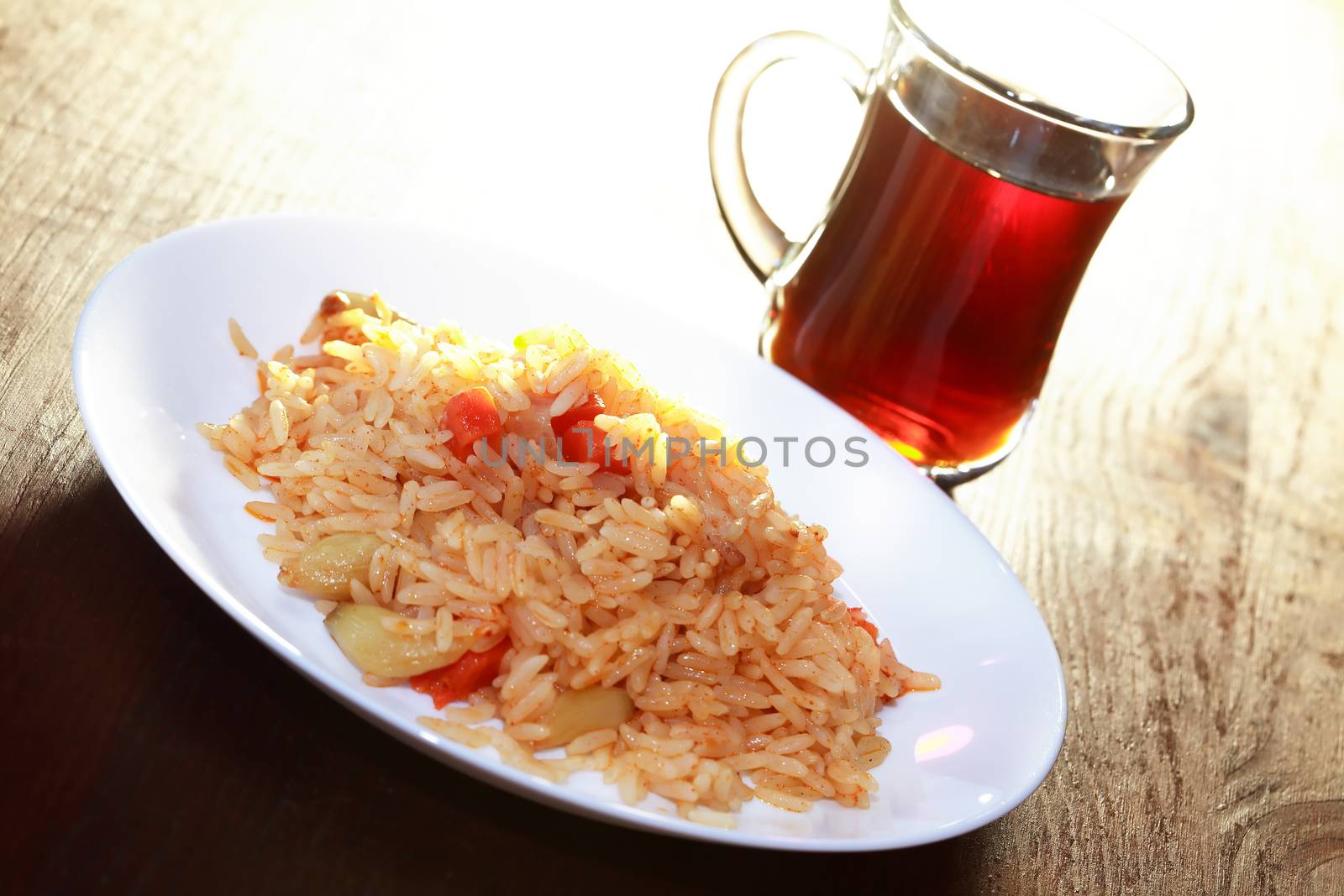 White plate with pilaf near cup of tea on wooden table