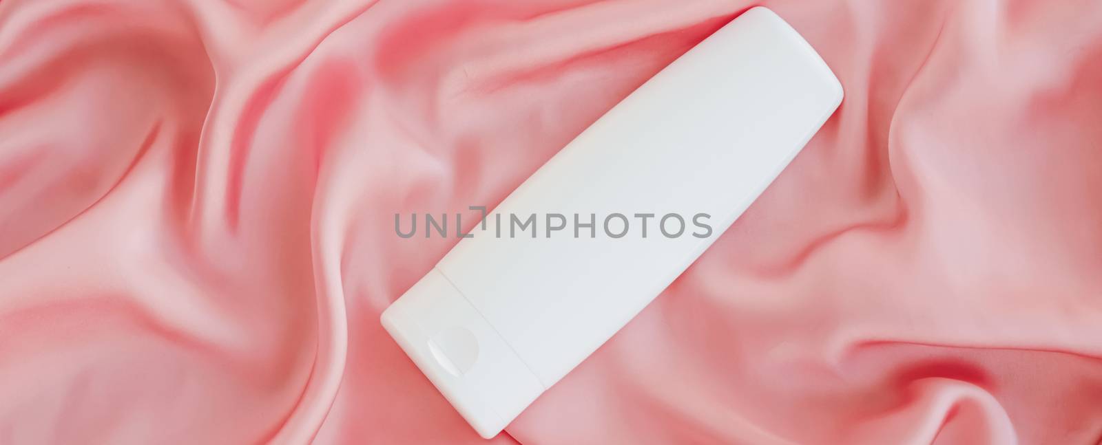 Blank label cosmetic container bottle as product mockup on pink silk background by Anneleven