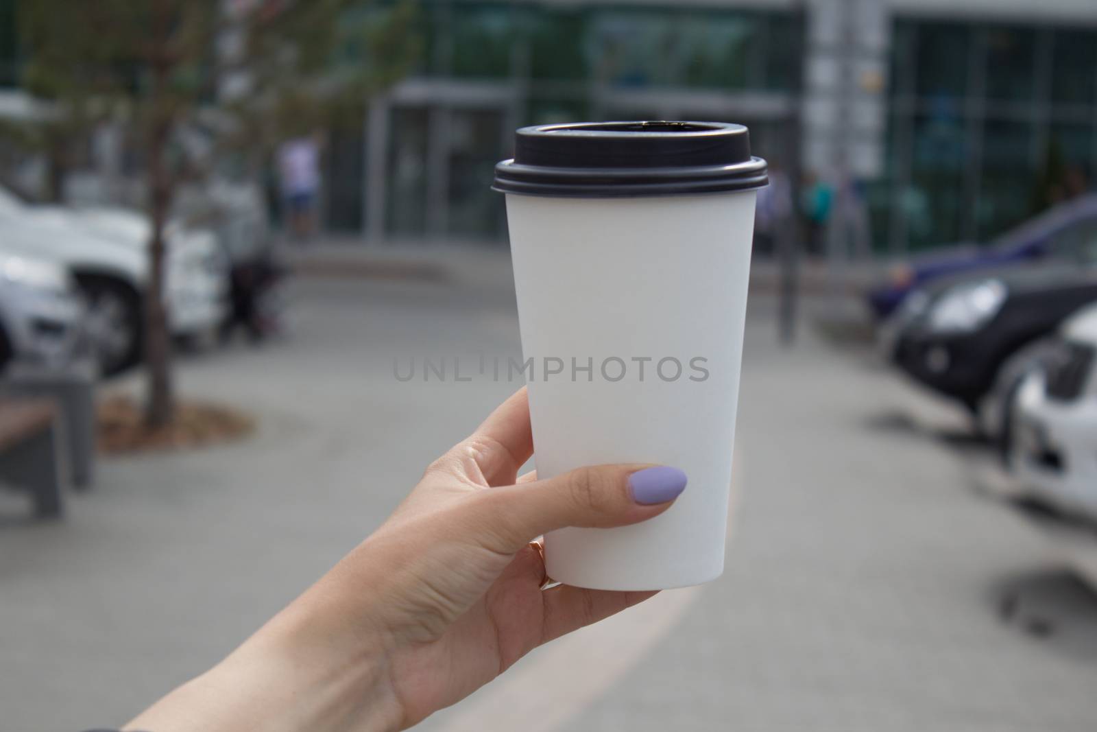 Breakfast and coffee theme: a woman's hand holding a white paper coffee Cup with a black plastic lid. by AnatoliiFoto