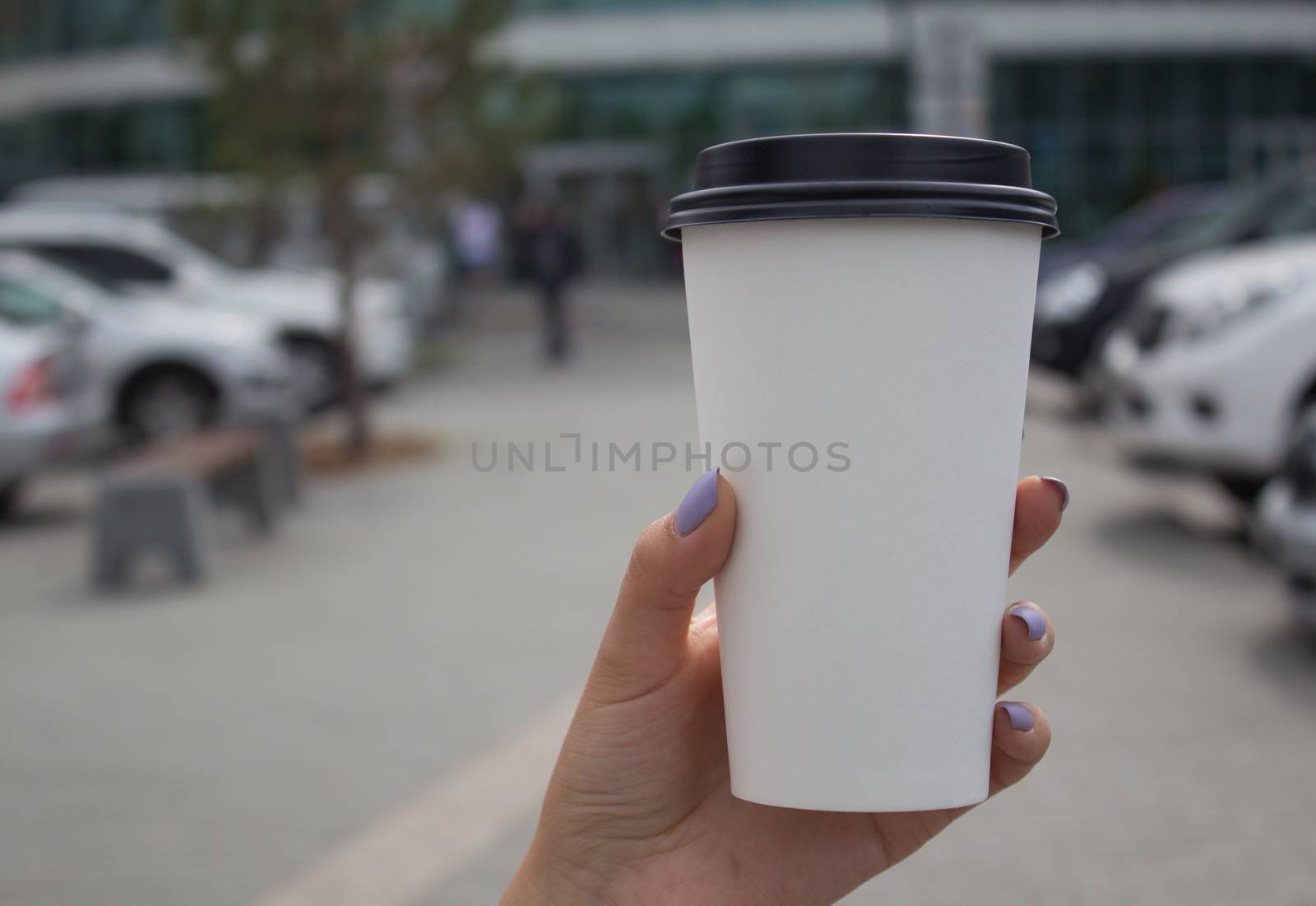 Breakfast and coffee theme: a woman's hand holding a white paper coffee Cup with a black plastic lid. Coffee advertising