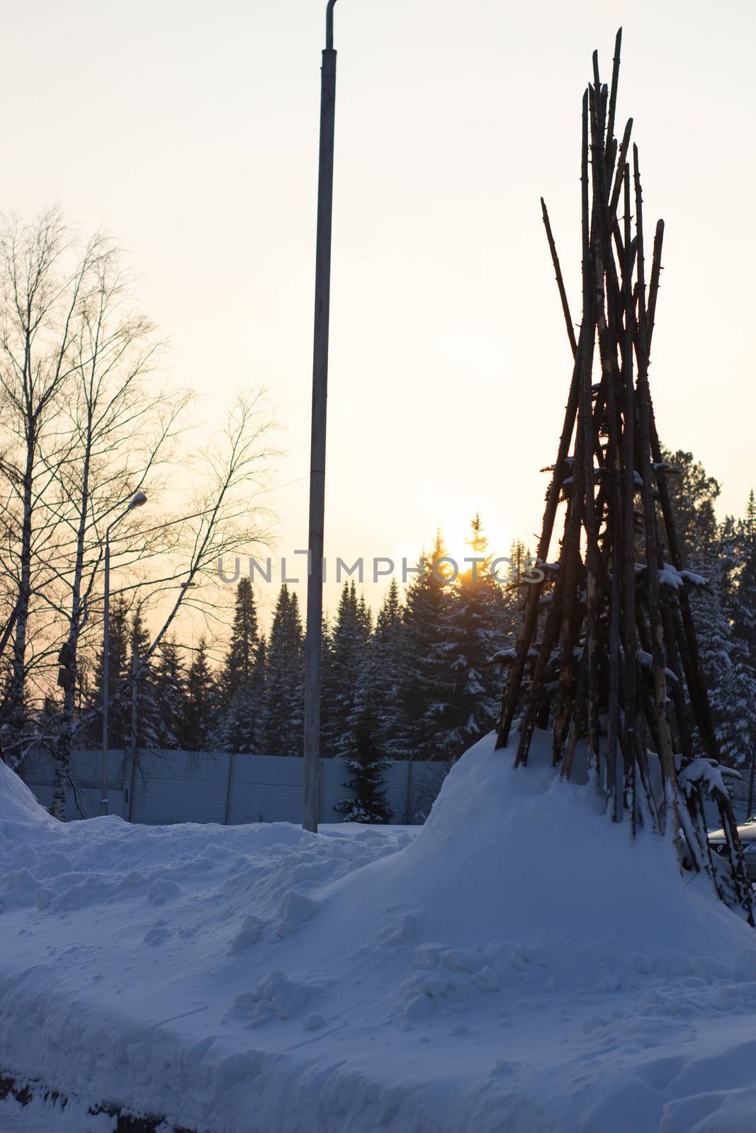Tipi posts stuck in the thick snow in the middle of winter surrounded by lush green pines.