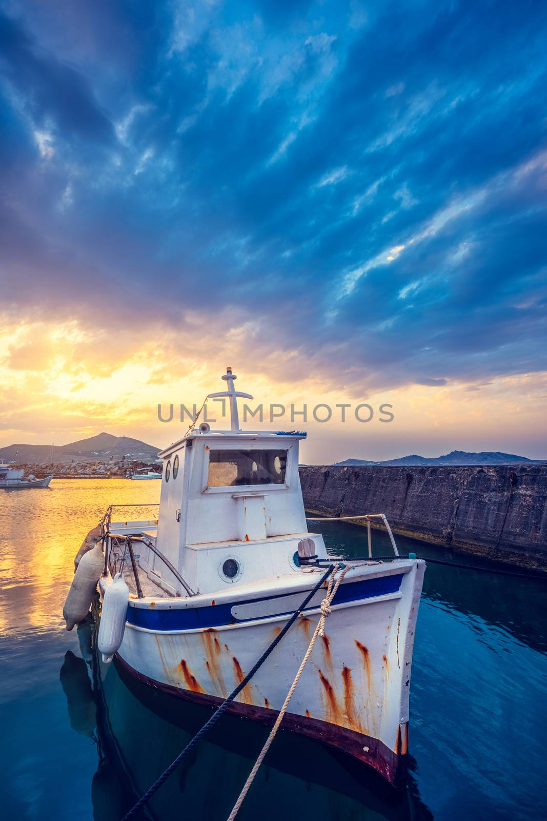 Old fishing boat in port of Naousa on sunset with dramatic sky. Paros lsland, Greece