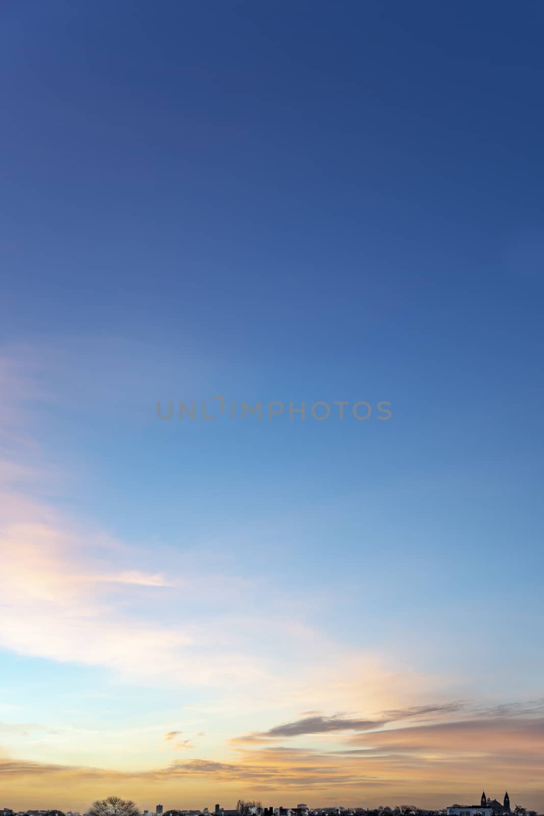 Portrait view of an early morning sky with tin and small clouds lighted by the vivid morning sunrise at the horizon