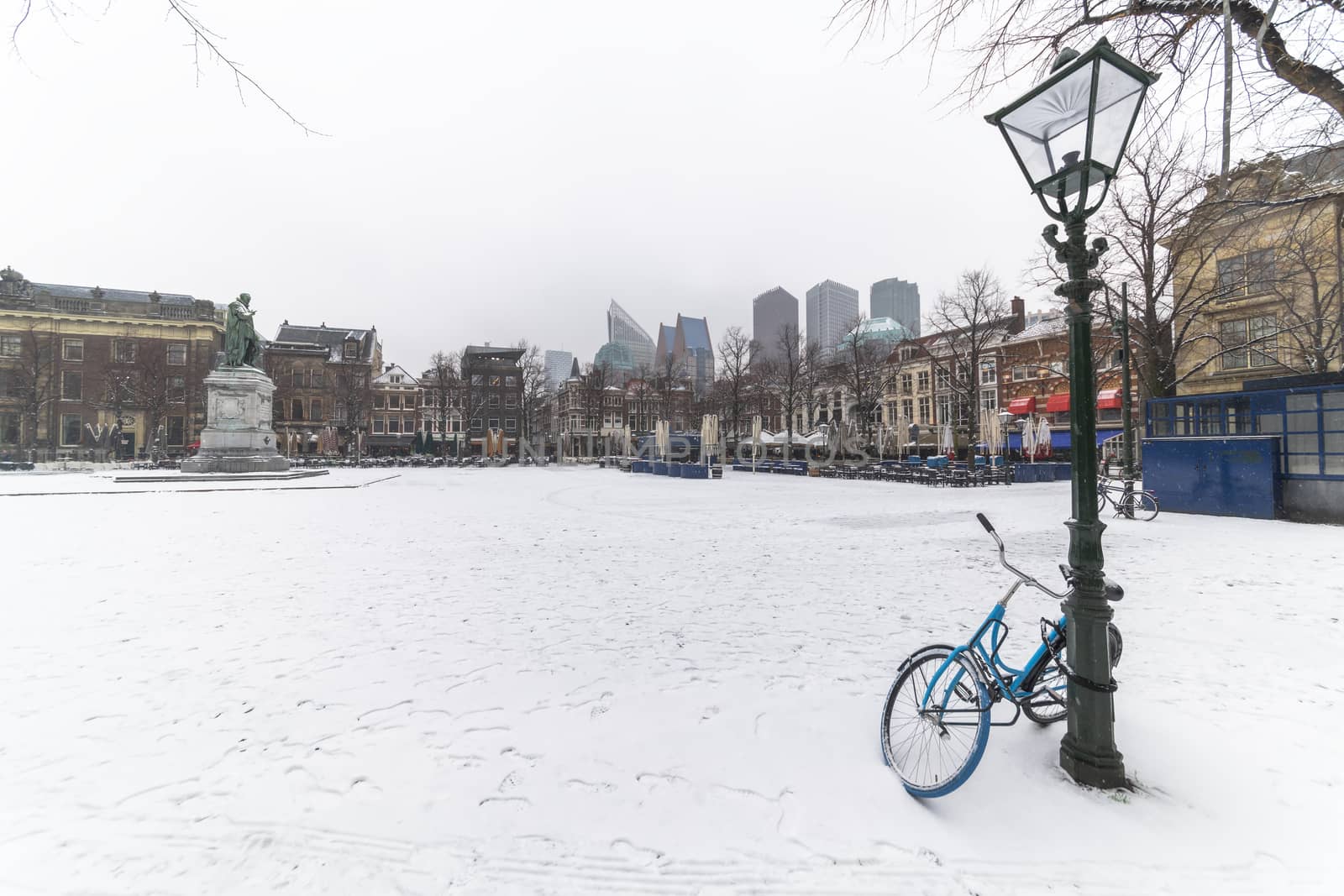 Bicycle locked with the lamp post at the central place covered by snow, Plein (Dutch), usually crowded with people getting diner and drink during the sunset and warm weather in The Hague, Netherlands by ankorlight