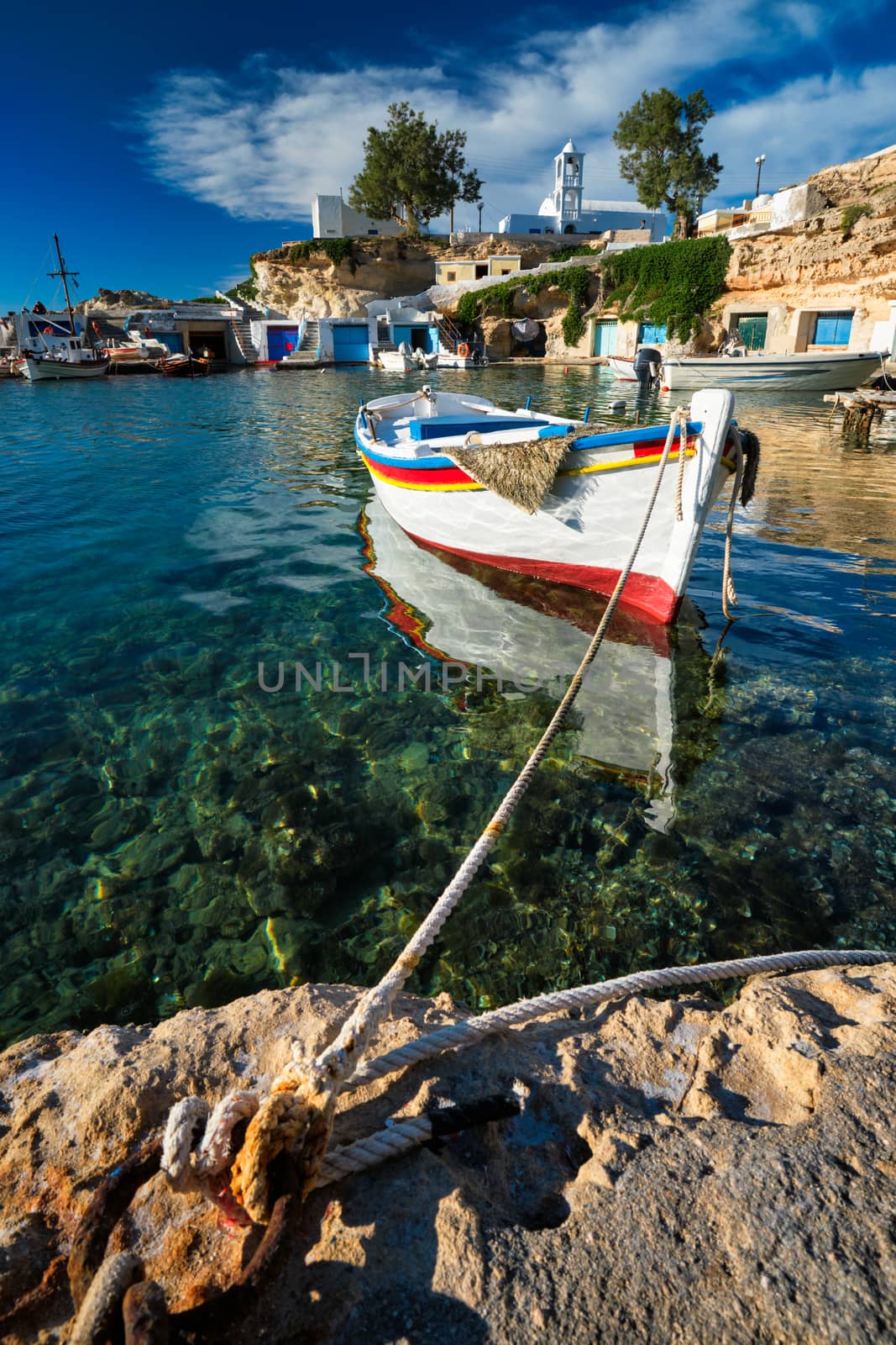 Fishing boats moored in crystal clear turquoise sea water in harbour in Greek fishing village of Mandrakia, Milos island, Greece. Horizontal camera pan