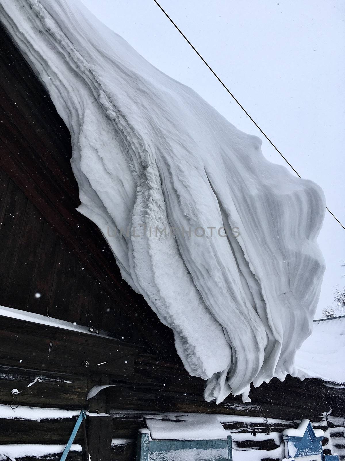 A lot of snow on the roof of the house and buildings. Winter in the country and in the city. The sun shines on the snow of the hemisphere curve, and the snow on the roof of the winter house is thick,