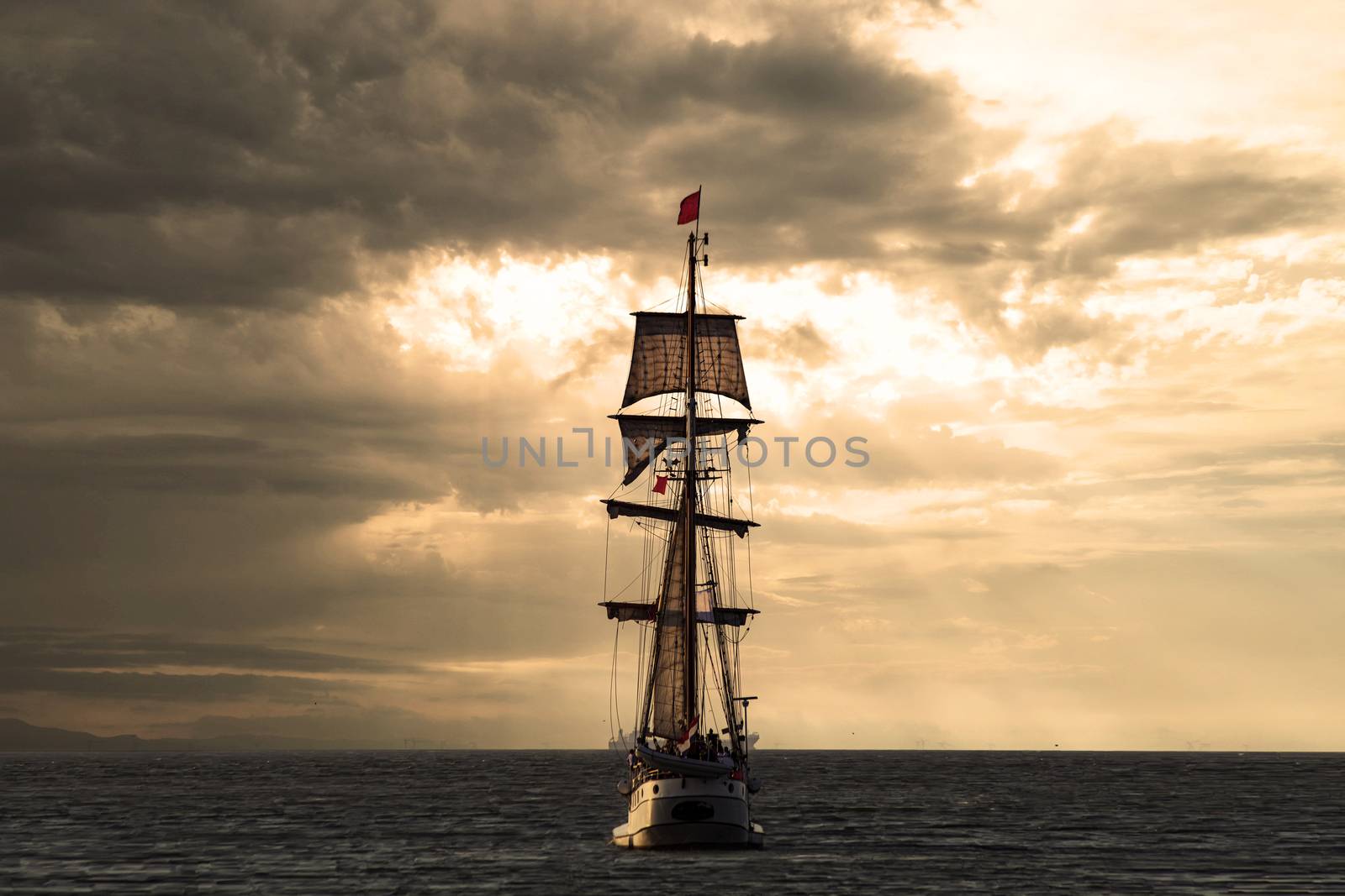 Antique tall ship, vessel leaving the harbor of The Hague, Scheveningen under a warm sunset and golden sky by ankorlight