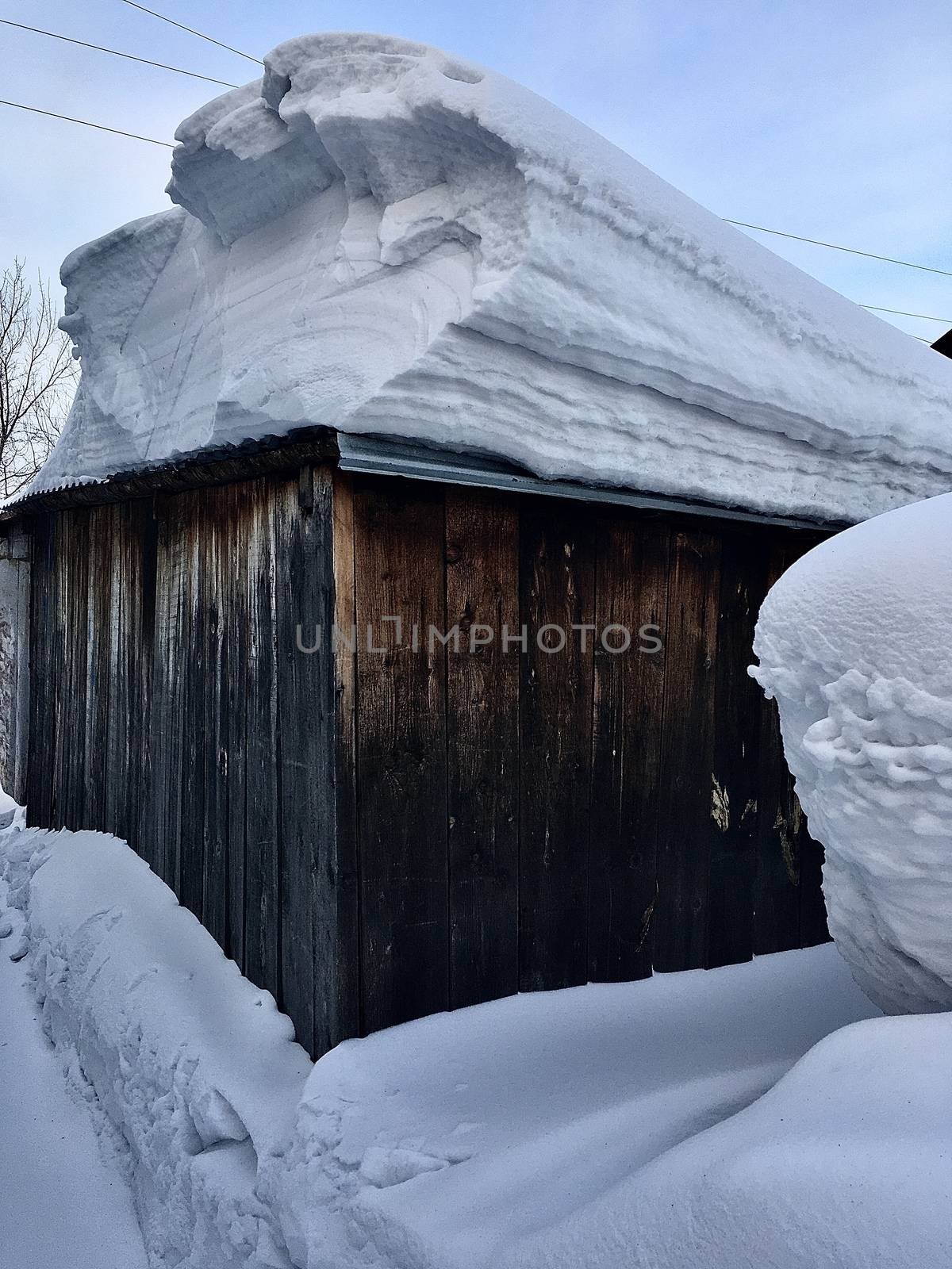 A lot of snow on the roof of the house and buildings. Winter in the country and in the city. The sun shines on the snow of the hemisphere curve, and the snow on the roof of the winter house is thick,