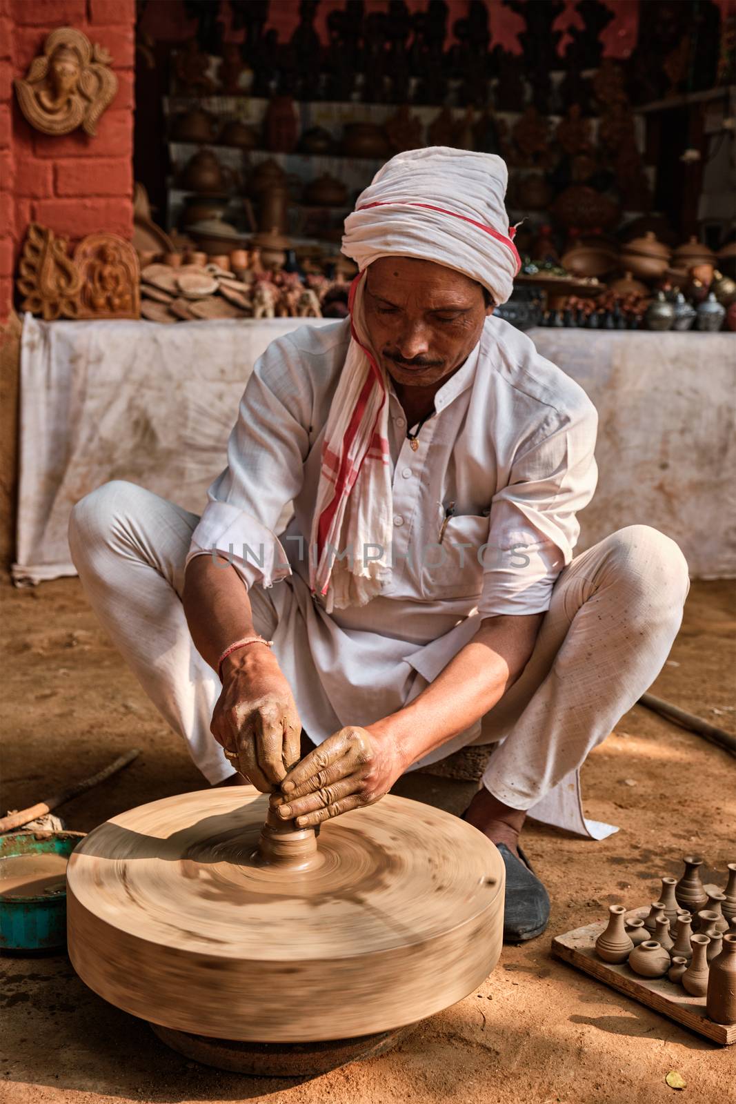 Indian potter at work: throwing the potter's wheel and shaping ceramic vessel and clay ware: pot, jar in pottery workshop. Experienced master. Handwork craft from Shilpagram, Udaipur, Rajasthan, India