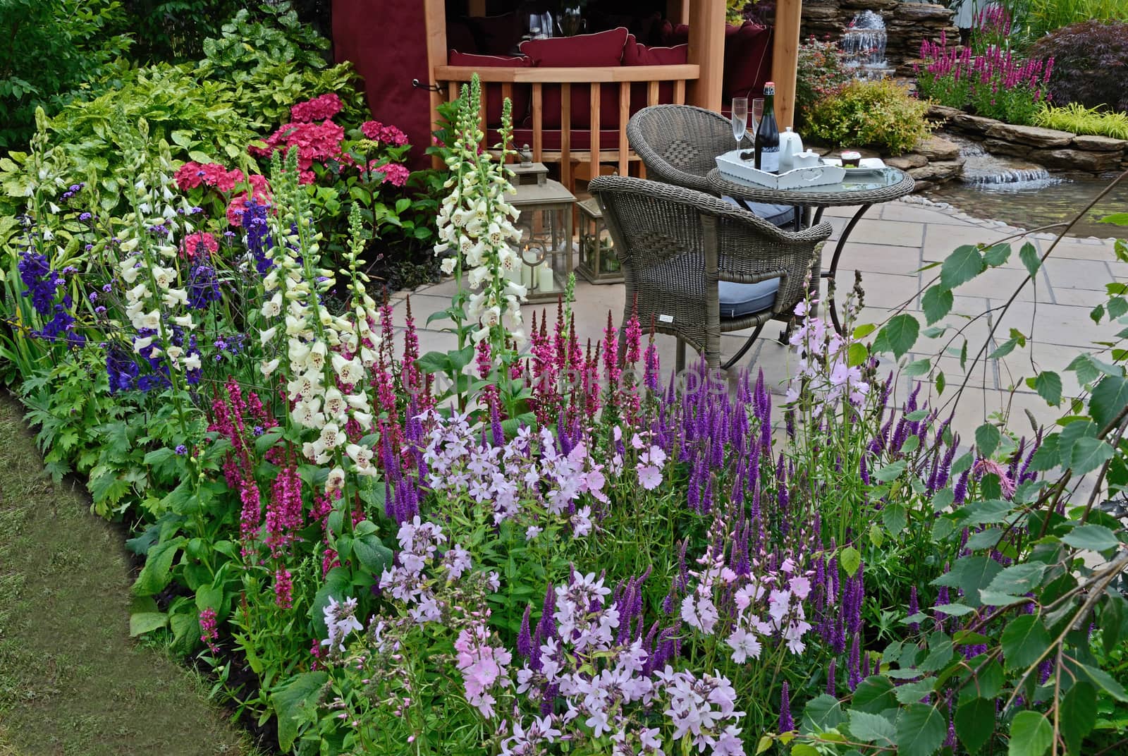 The patio area of an aquatic garden with colourful flower border with Summer House and outdoor eating on the terrace,
