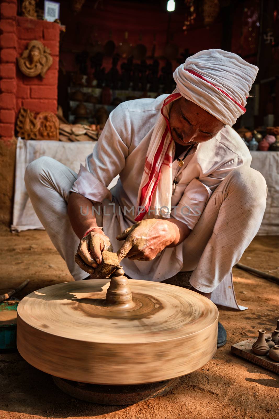 Indian potter at work: throwing the potter's wheel and shaping ceramic vessel and clay ware: pot, jar in pottery workshop. Experienced master. Handwork craft from Shilpagram, Udaipur, Rajasthan, India