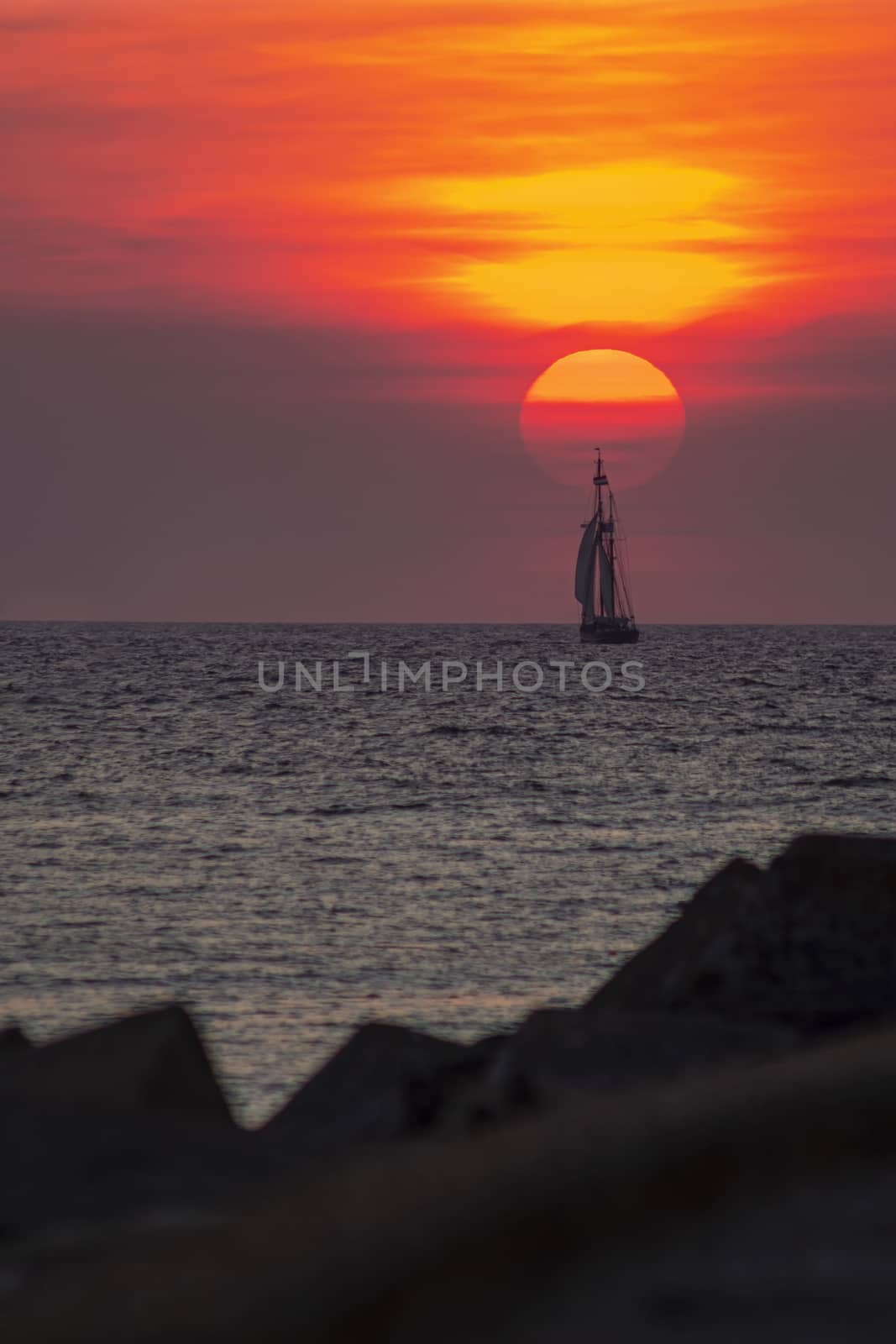 Tall ship, vessel, sailing and preparing the enter inside the harbor of Scheveningen at the vivid sunset moment, The Hague, Netherlands