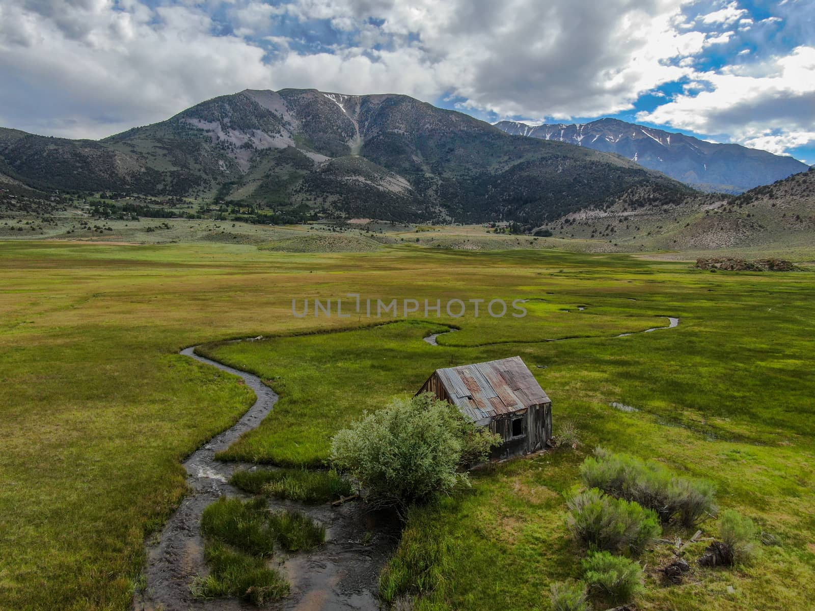 Aerial view of abandoned little small wooden house barn next small river in the green valley of a mountain, Aspen Spring, Mono County, California, USA. 