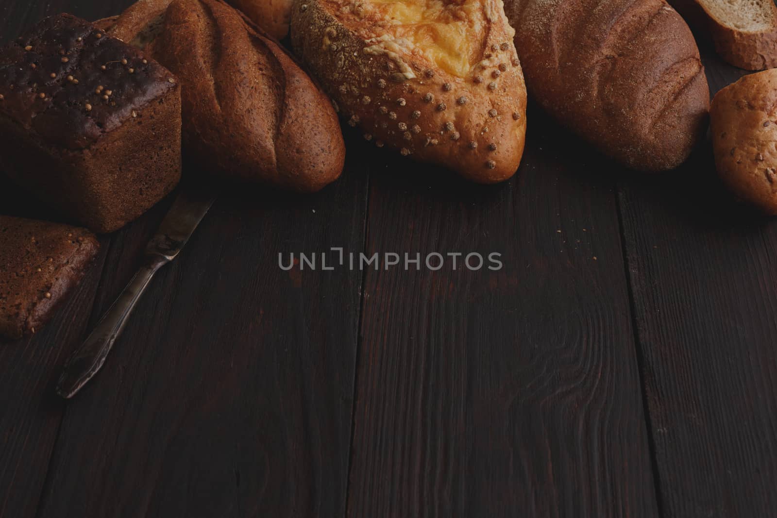 Different wholegrain breads on burnished wooden table. Elevated view, chiaroscuro styled