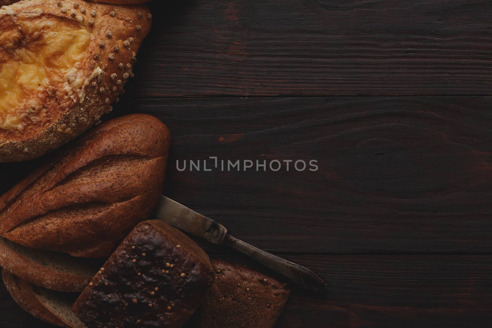 Different wholegrain breads on burnished wooden table. Flat lay, above view, chiaroscuro styled