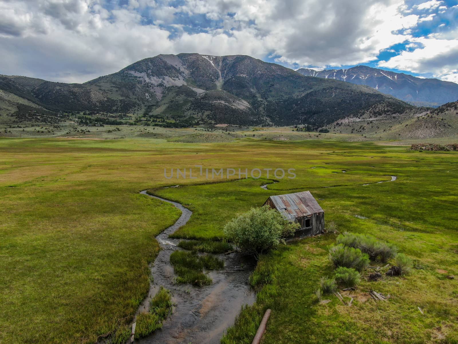 Aerial view of abandoned little small wooden house barn next small river in the green valley of a mountain, Aspen Spring, Mono County, California, USA. 