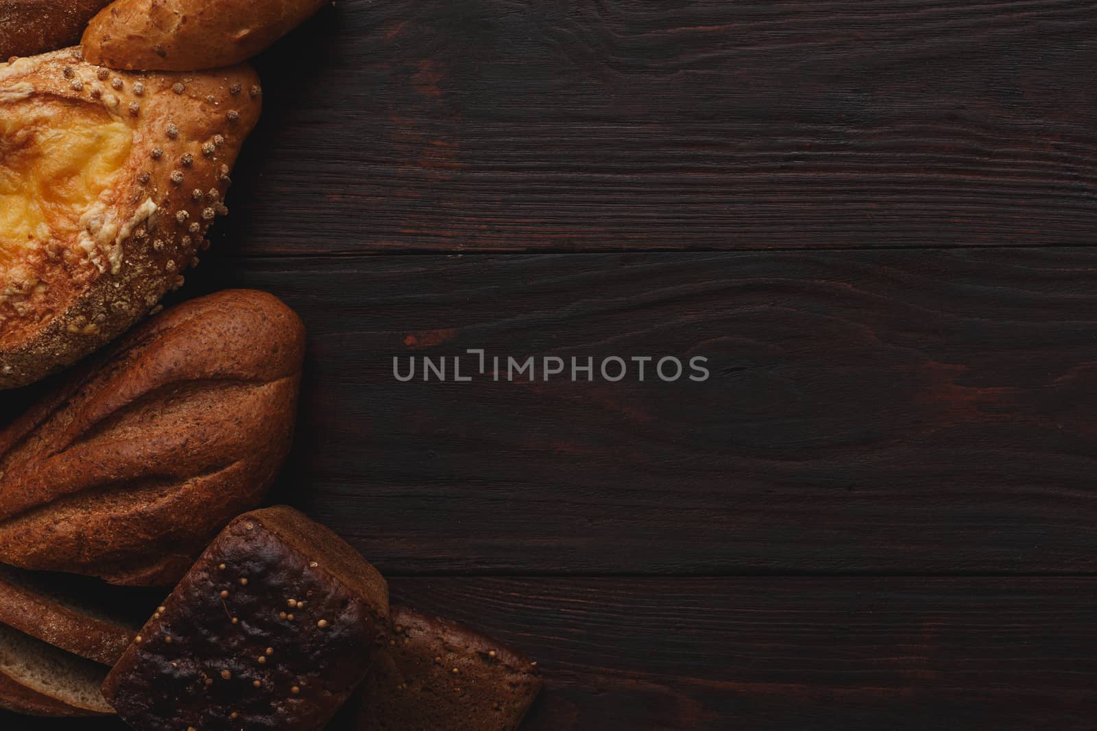 Different wholegrain breads on burnished wooden table. Flat lay, above view, chiaroscuro styled