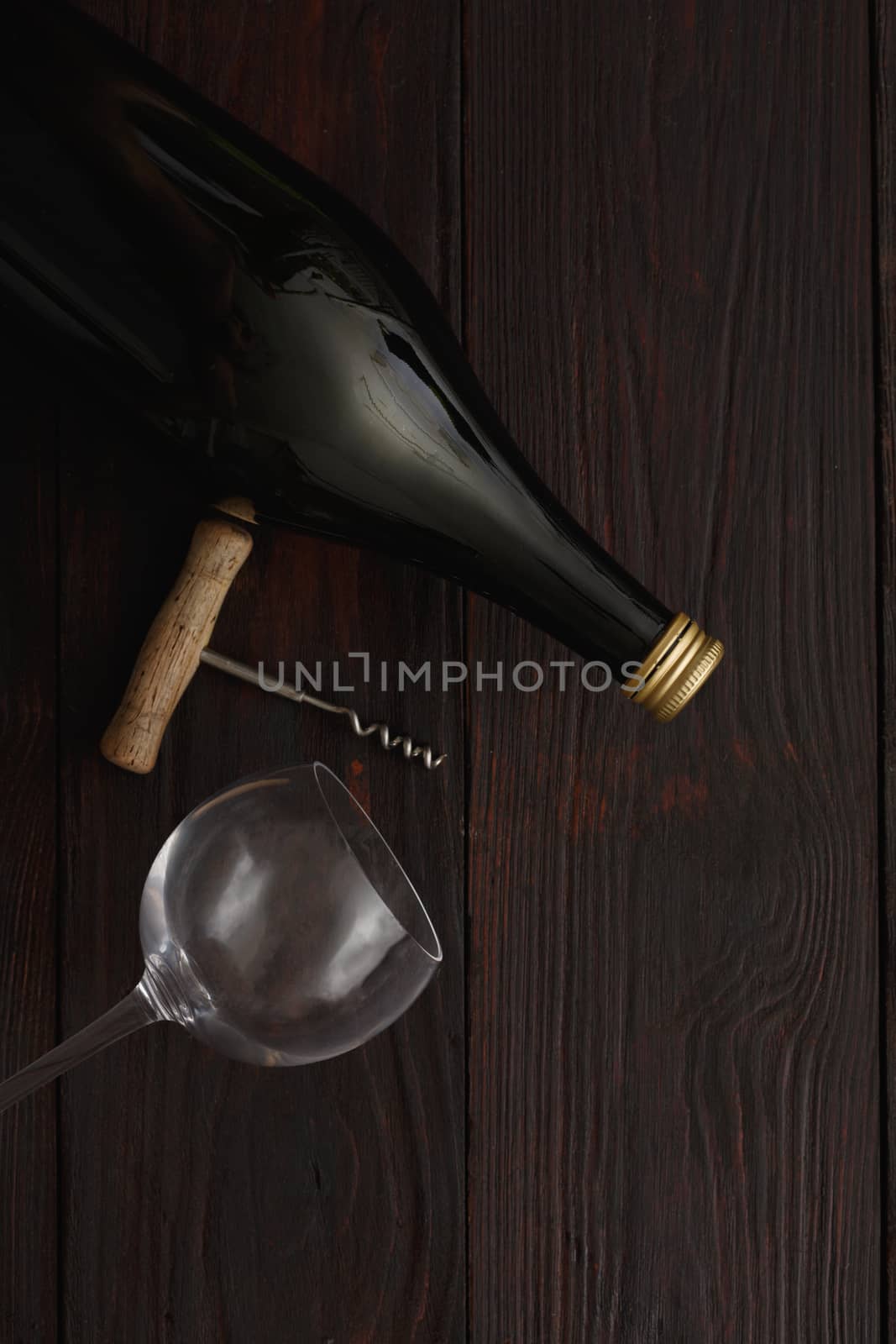 Bottle of red wine next to to empty glass with corkscrew on wooden table. Flat lay, above view, copy space,Chiaroscuro styled