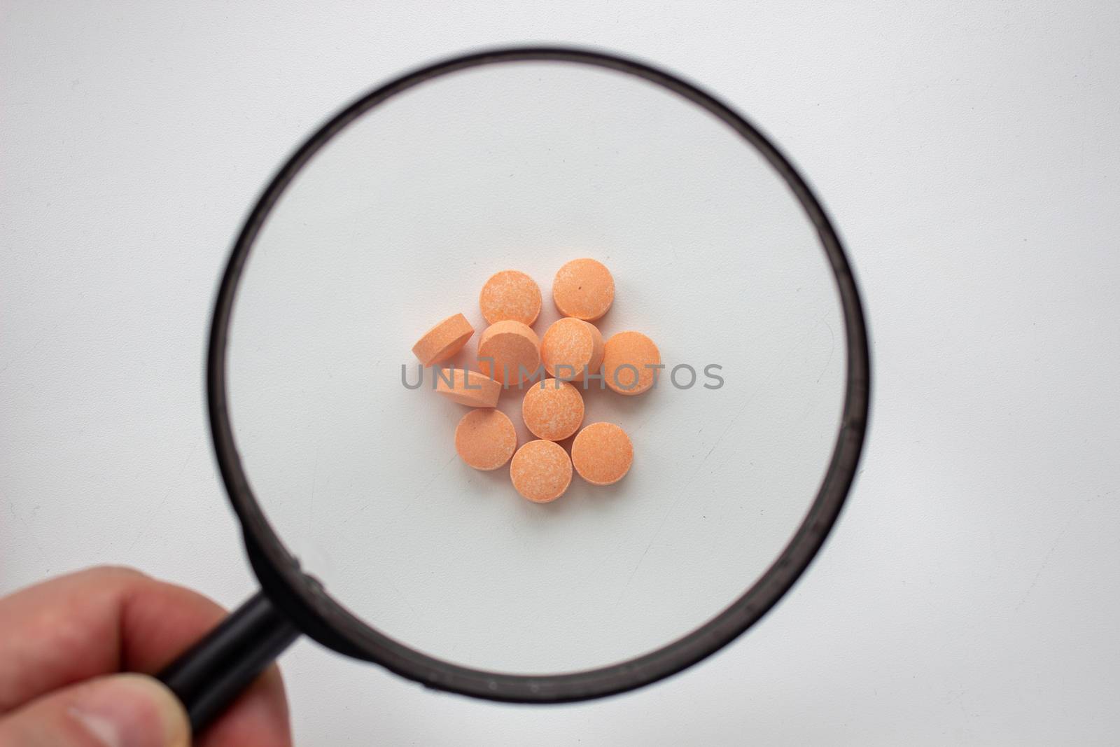 Medical tablets under a magnifying glass on a white background. by AnatoliiFoto