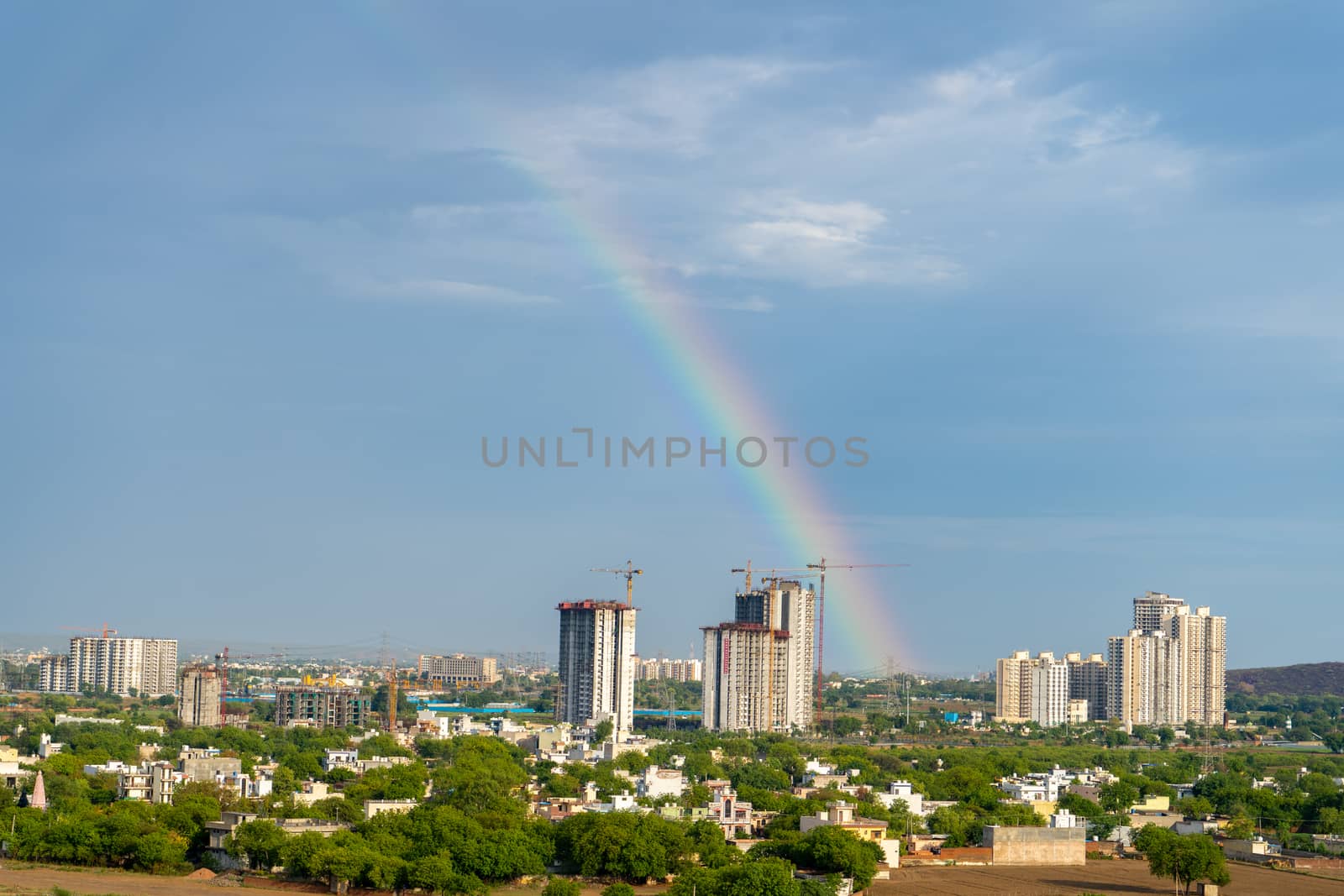 Aerial cityscape shot of buildings in gurgaon delhi noida with a rainbow behind them on a monsoon day by Shalinimathur