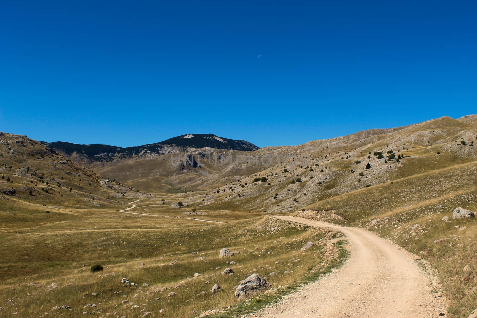 Old mountain road, rocky landscape, mountain top in the background with blue sky and moon. Bjelasnica Mountain, Bosnia and Herzegovina. by mahirrov