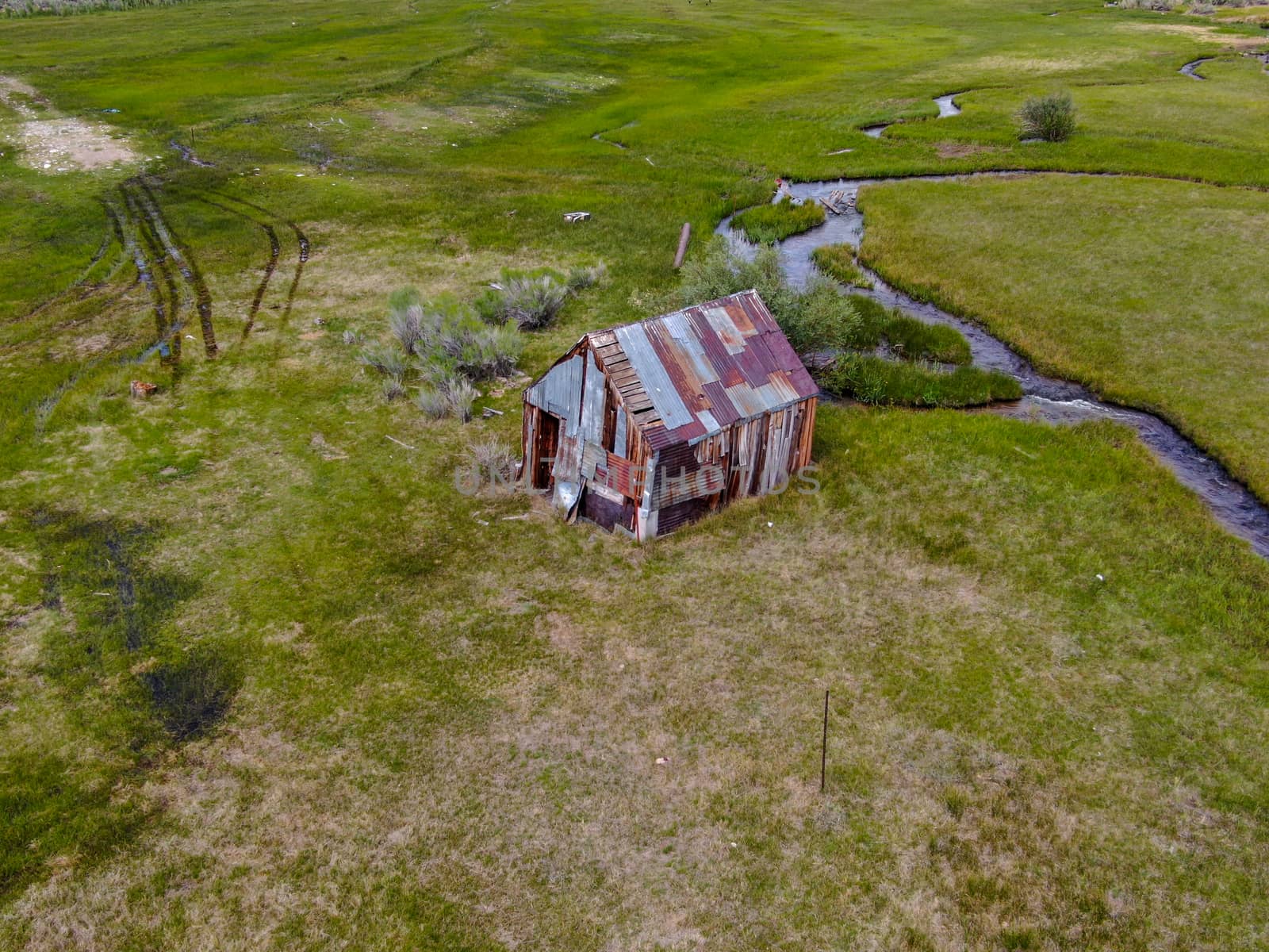 Aerial view of abandoned little small wooden house barn next small river in the green valley of a mountain, Aspen Spring, Mono County, California, USA. 