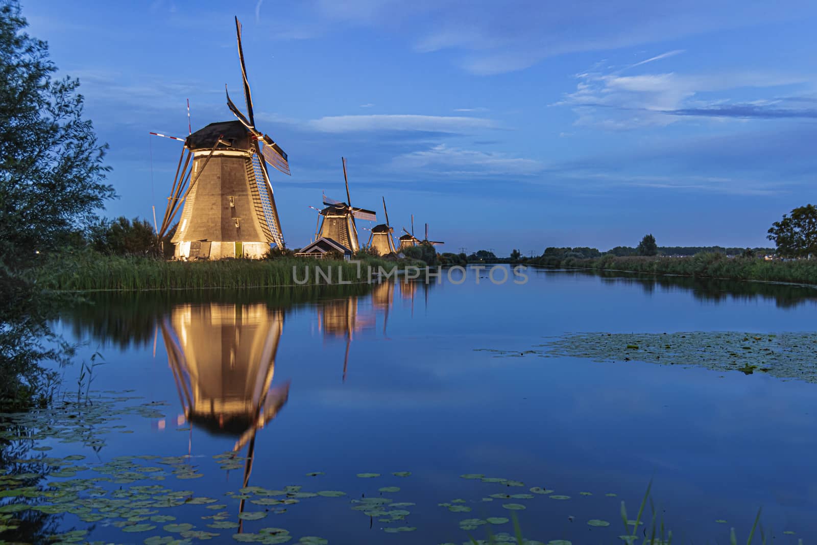 Illuminated windmill reflected on the calm canal water during the bleu hour sunset in Alblasserdam city, Netherlands