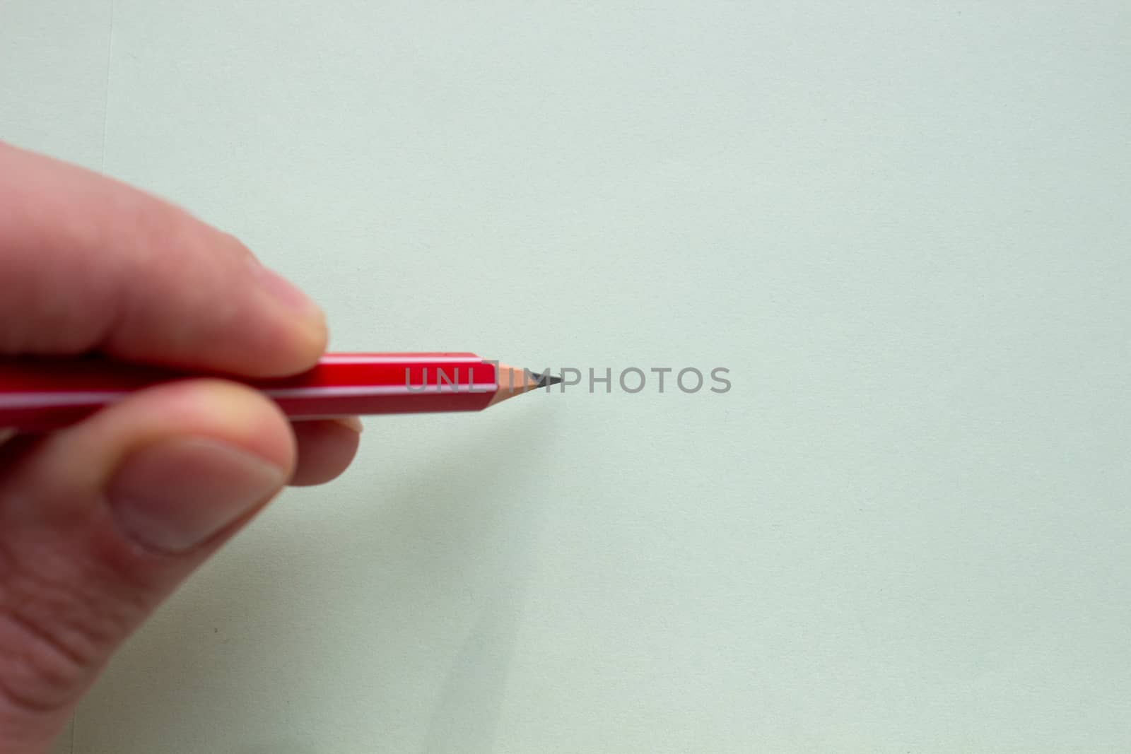 A man holds a red pencil on a light paper with his fingers. by AnatoliiFoto