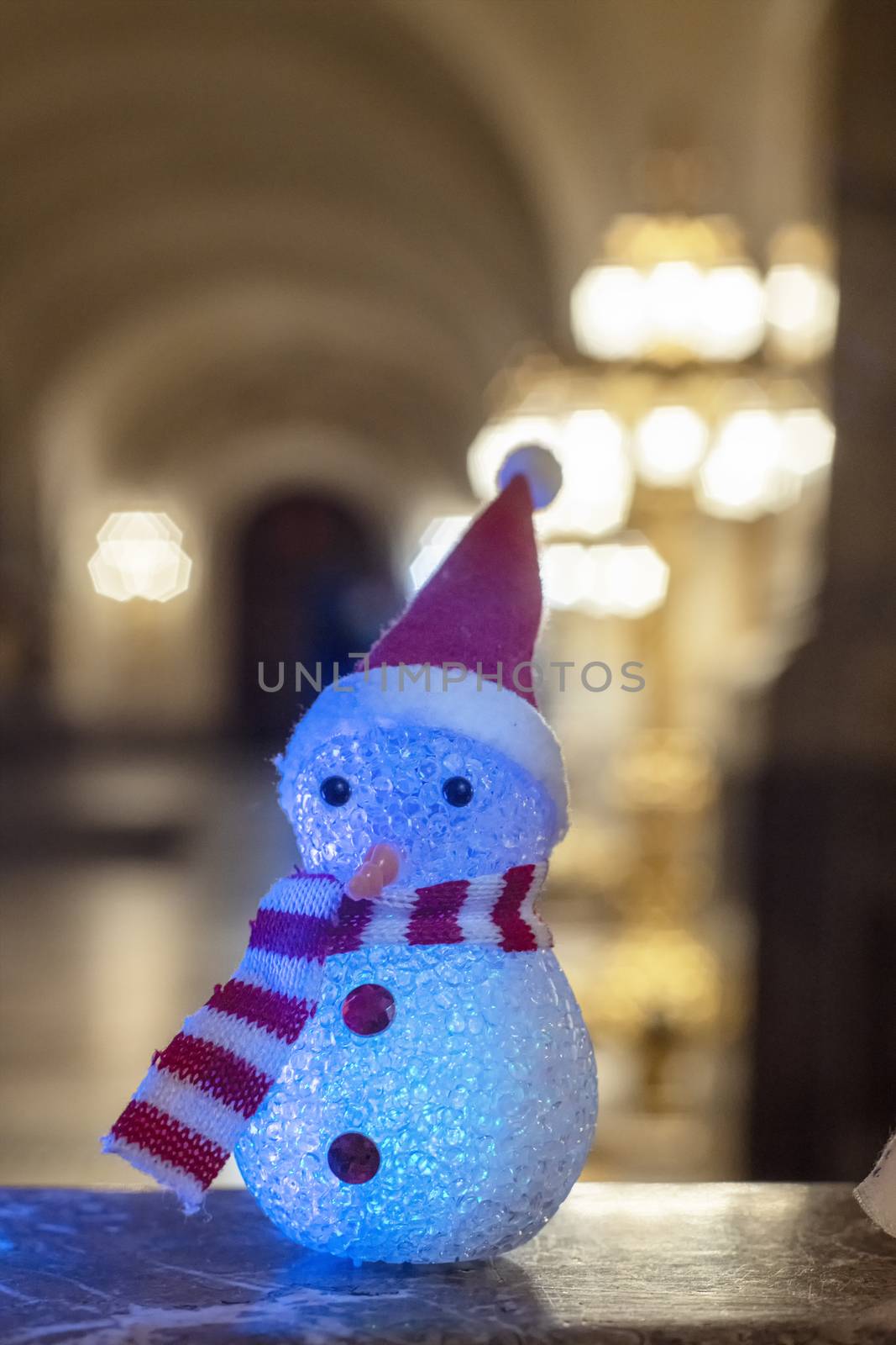 Little snowman wearing a rainbow scarf and hat against a golden light bokeh waiting for Christmas time and gifts